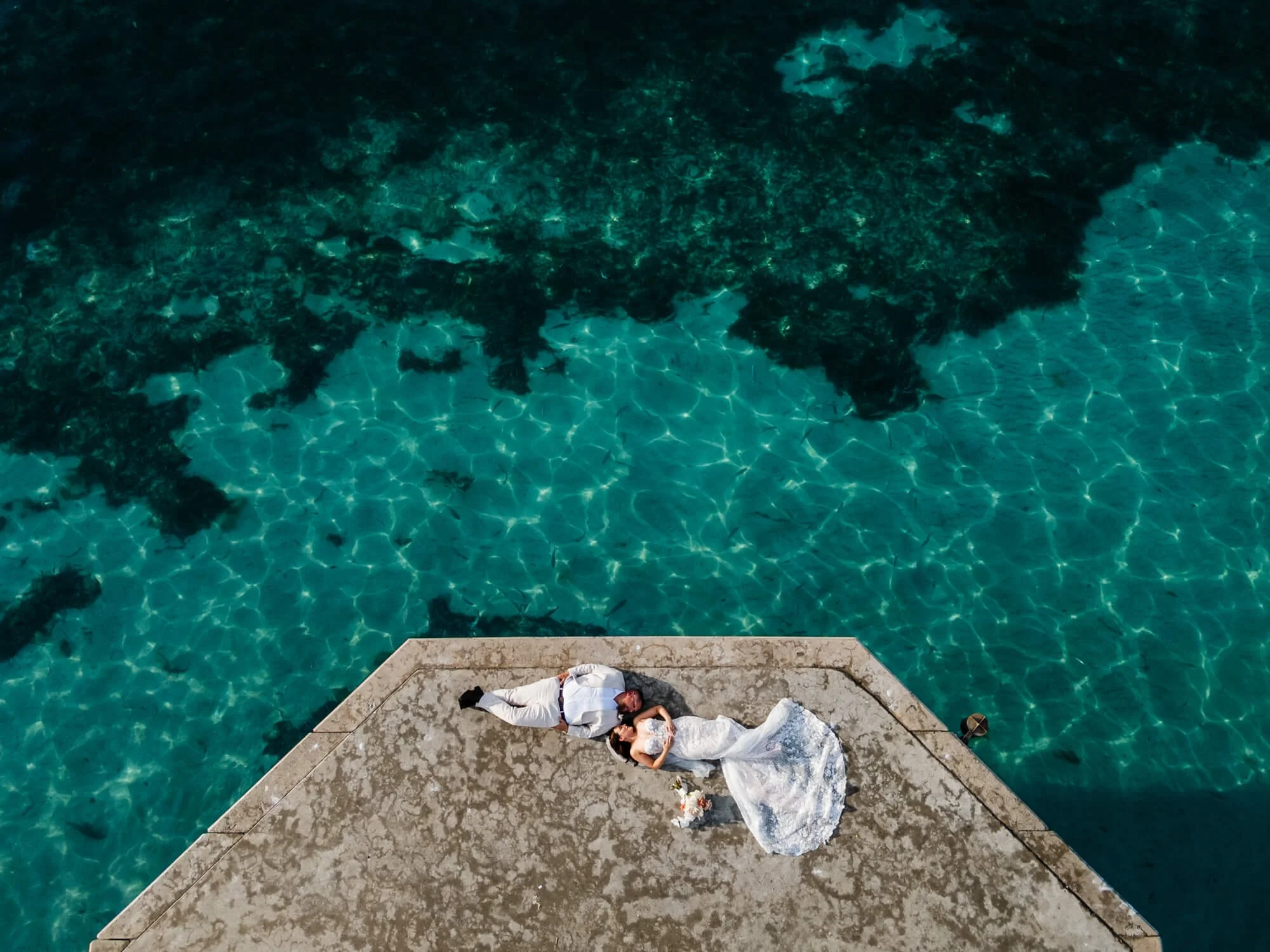 Aerial drone view of the bride and groom sitting at the end of a jetty over the turquoise waters of Shoal Bay, Port Stephens.