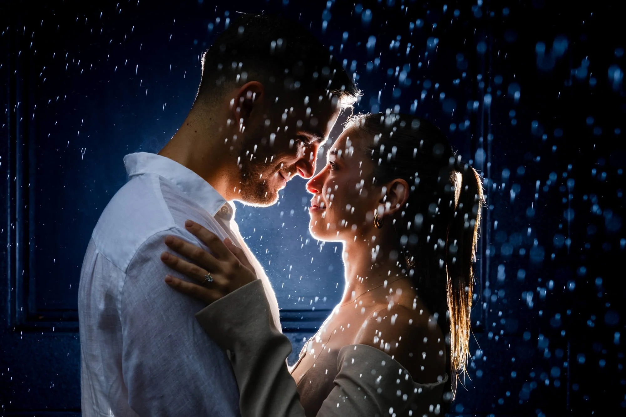 Couple sharing a close, almost-kissing moment in the dark as sparkles of light fall around them, a backlit portrait against a deep navy background, Bobs Farm, Port Stephens.