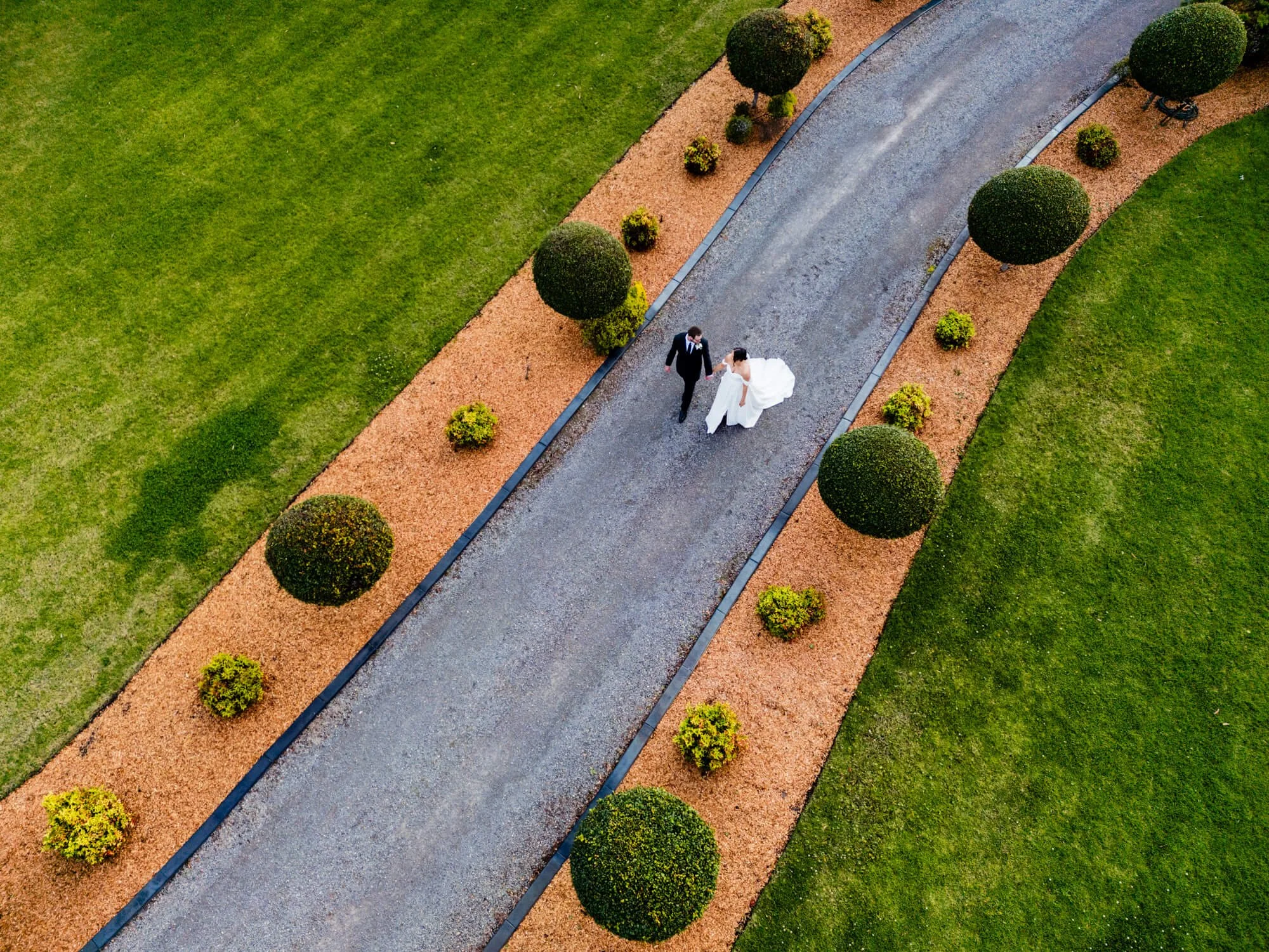 Aerial drone view of the bride and groom walking along a manicured garden path at Heaven Gardens, Salt Ash, Port Stephens.