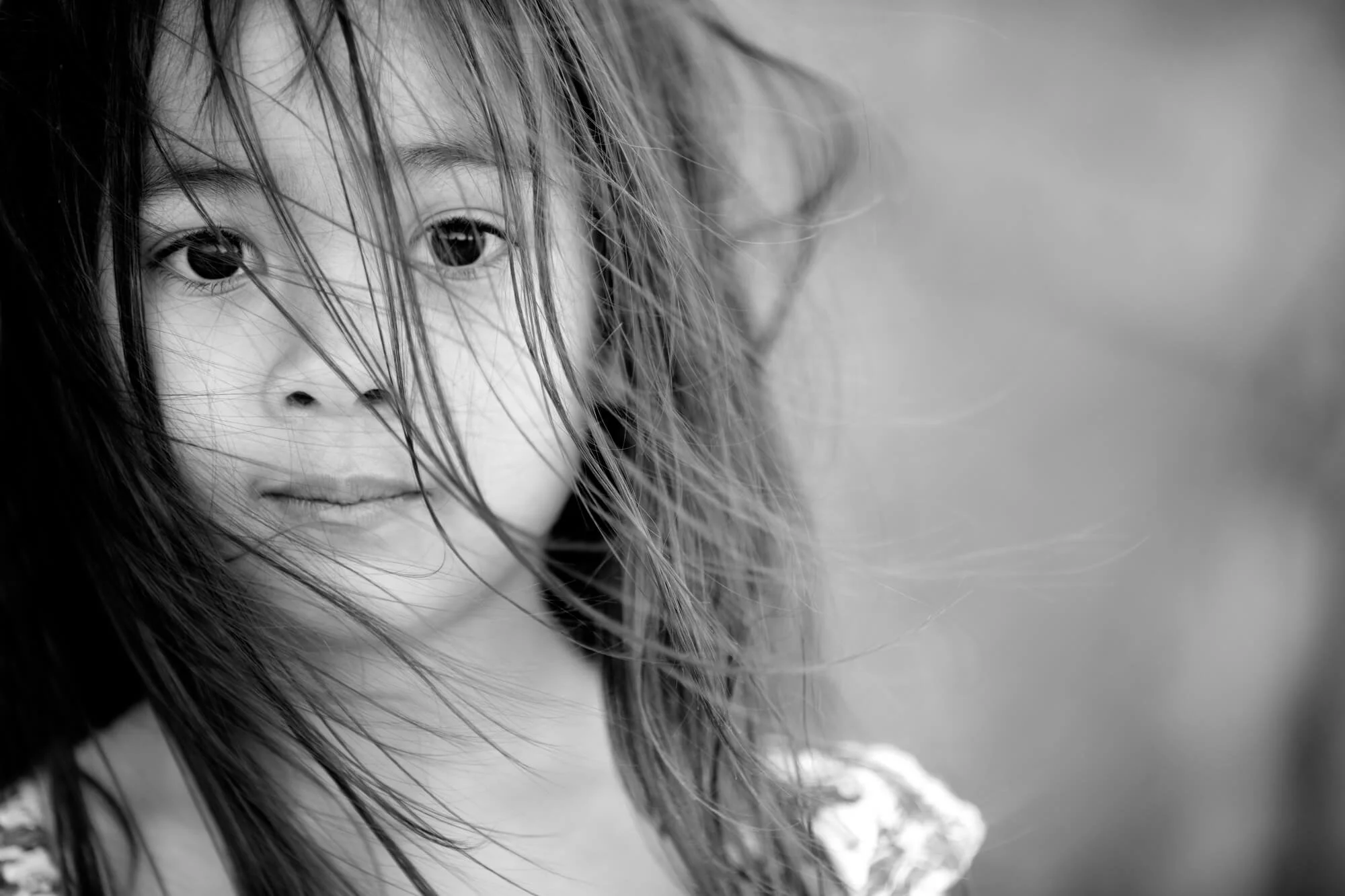 Black and white close-up portrait of a girl with wind-swept hair looking into the camera, Birubi Beach, Anna Bay, Port Stephens.