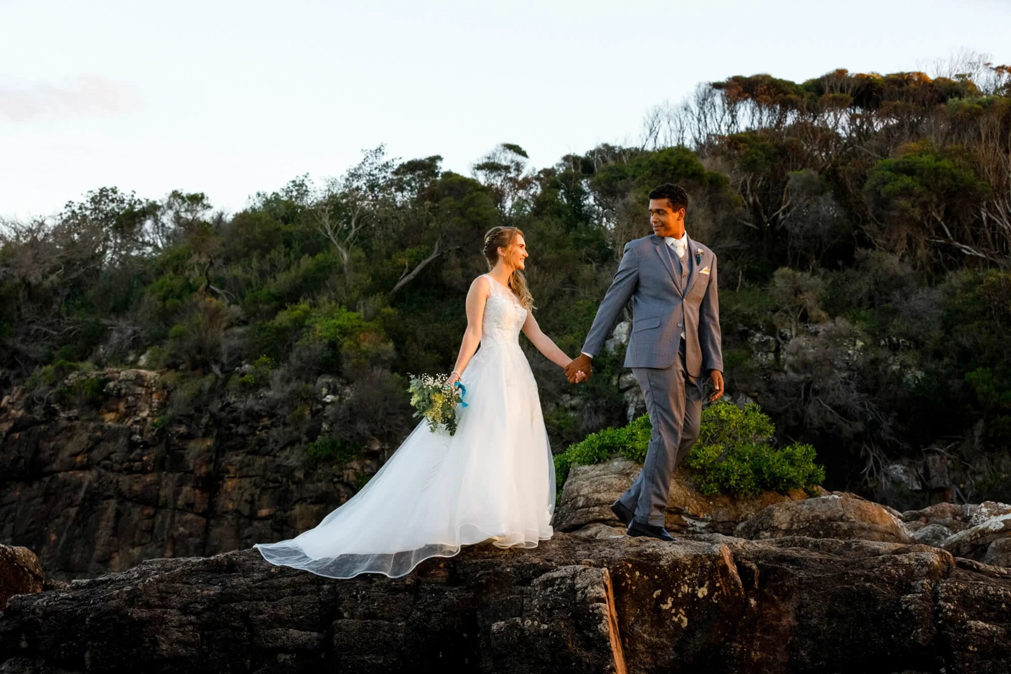 Bride and groom hold hands on the rugged rocky headland at Barry Park, Fingal Bay, Port Stephens.