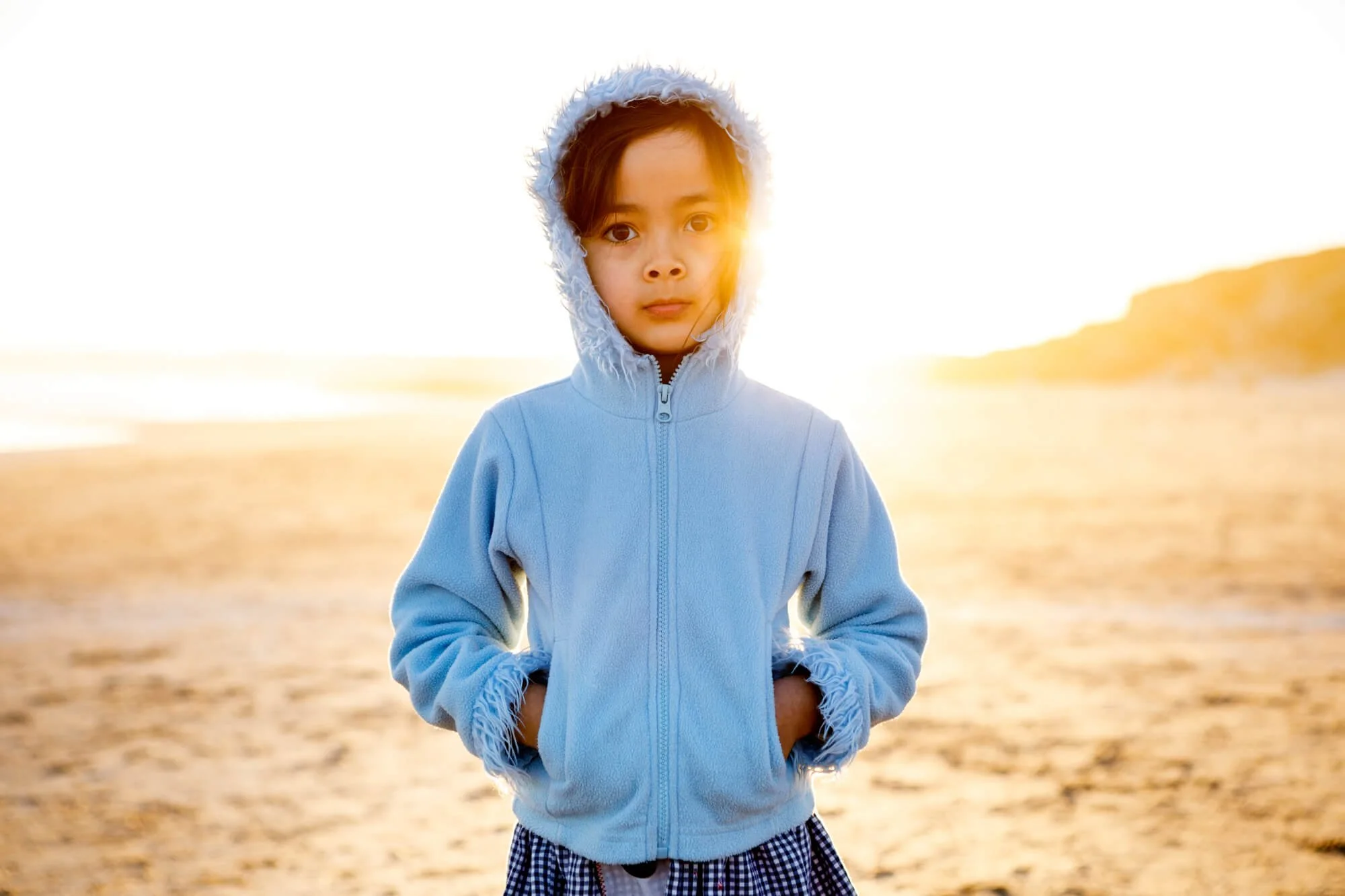 Portrait of a young child in a blue hooded jacket on the beach with golden sunset light glowing behind them, Birubi Beach, Anna Bay, Port Stephens..