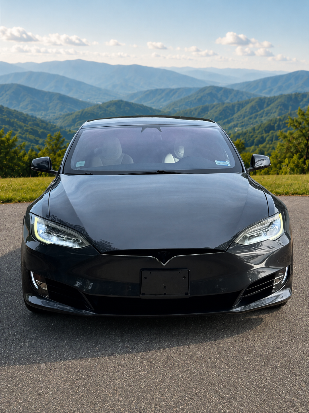 Black Tesla Model 3 car parked on the side of the road with a backdrop of green mountains and a partly cloudy sky.
