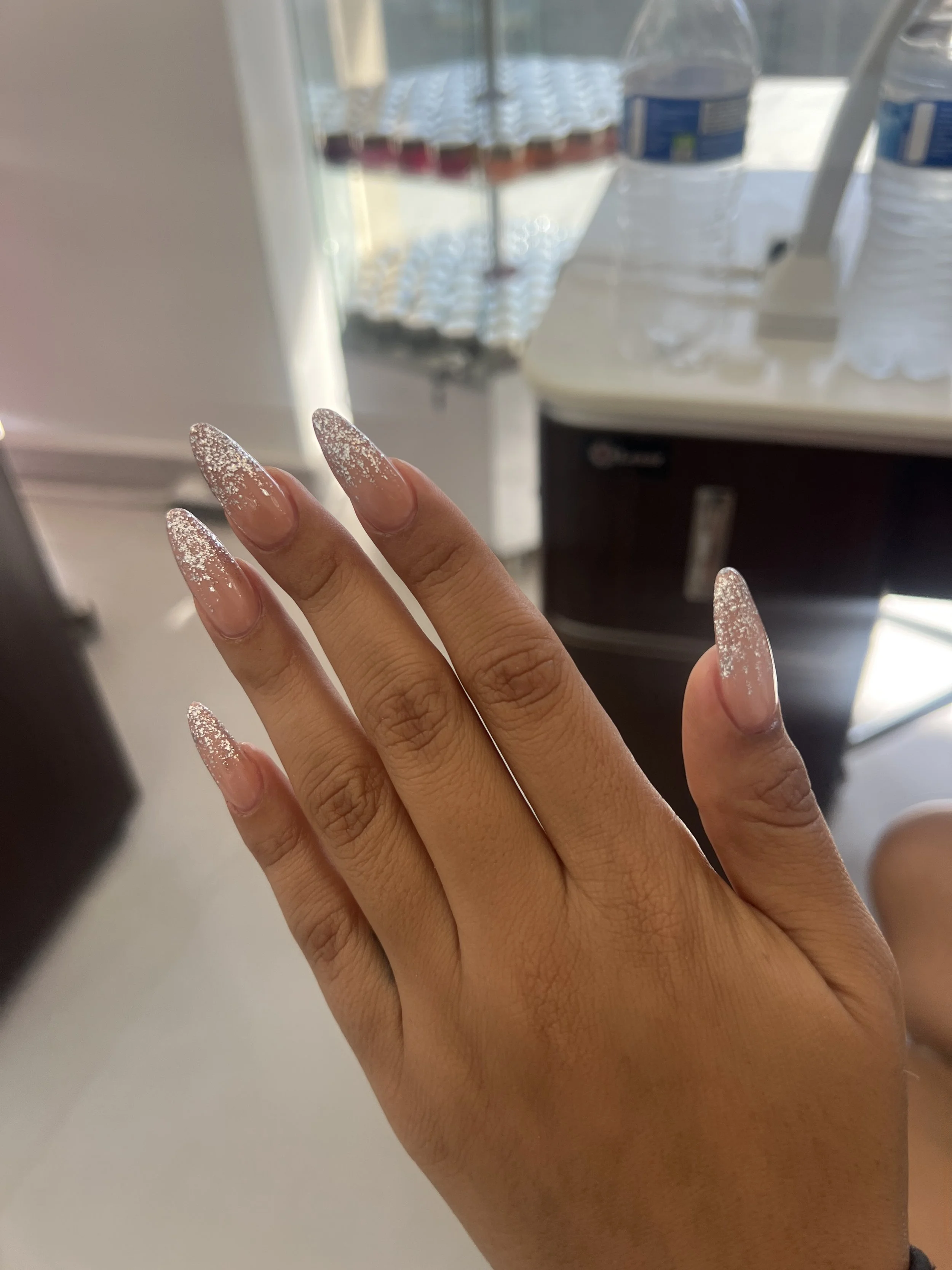Mano con uñas decoradas con brillo y diseño de línea en colores rosado y transparente.