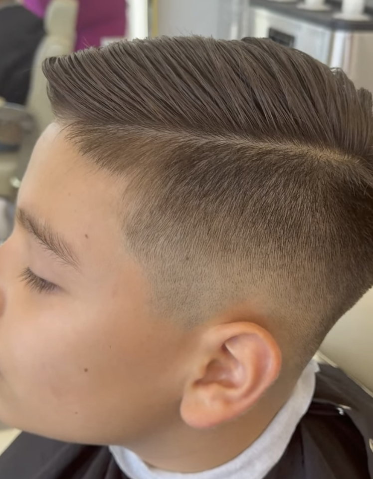 Joven con estilo de corte de cabello moderno, con cabello largo en la parte superior y estilos cortos en los lados, en un entorno de barbería.