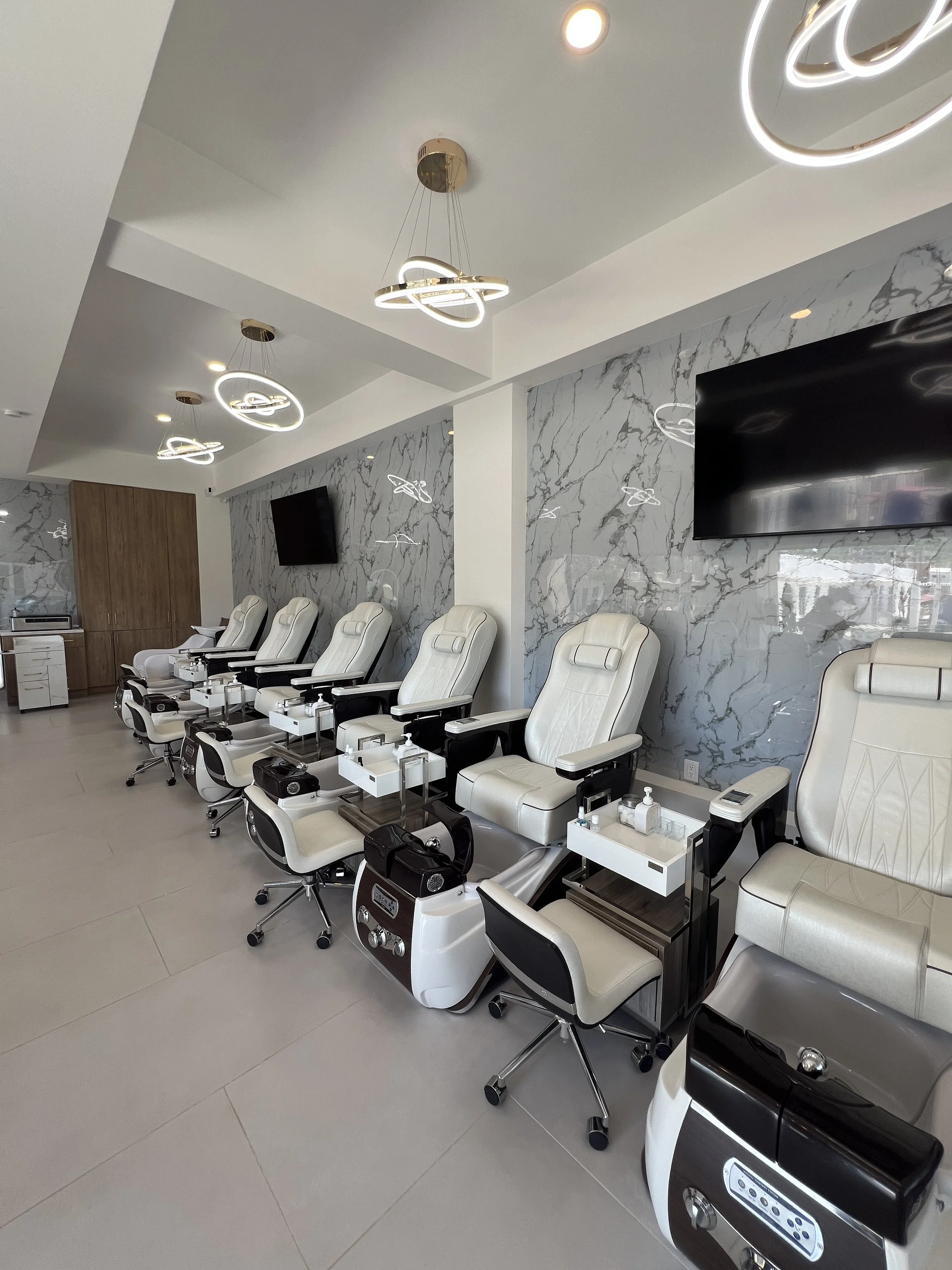 Seguidilla de sillas blancas con escritorios y máquinas de manicura en un salón moderno, con paredes de mármol y luces decorativas en el techo.