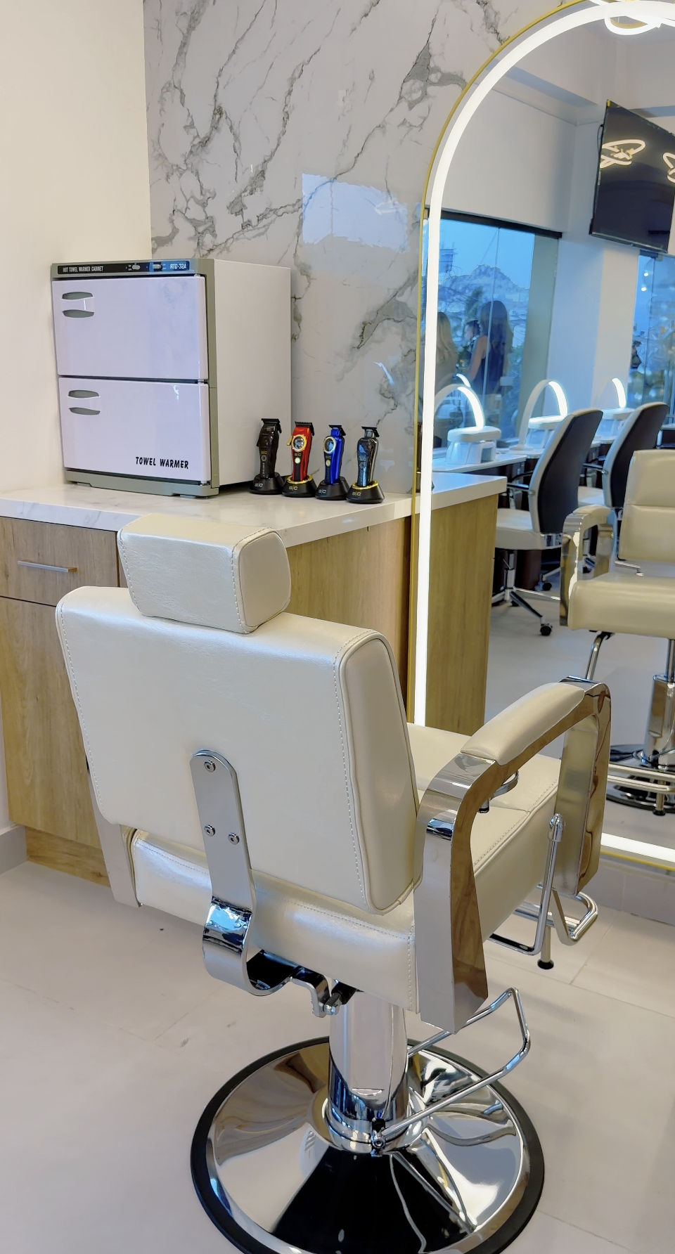 Silla de peluquería blanca en un salón de belleza, con espejos y televisores a la vista.