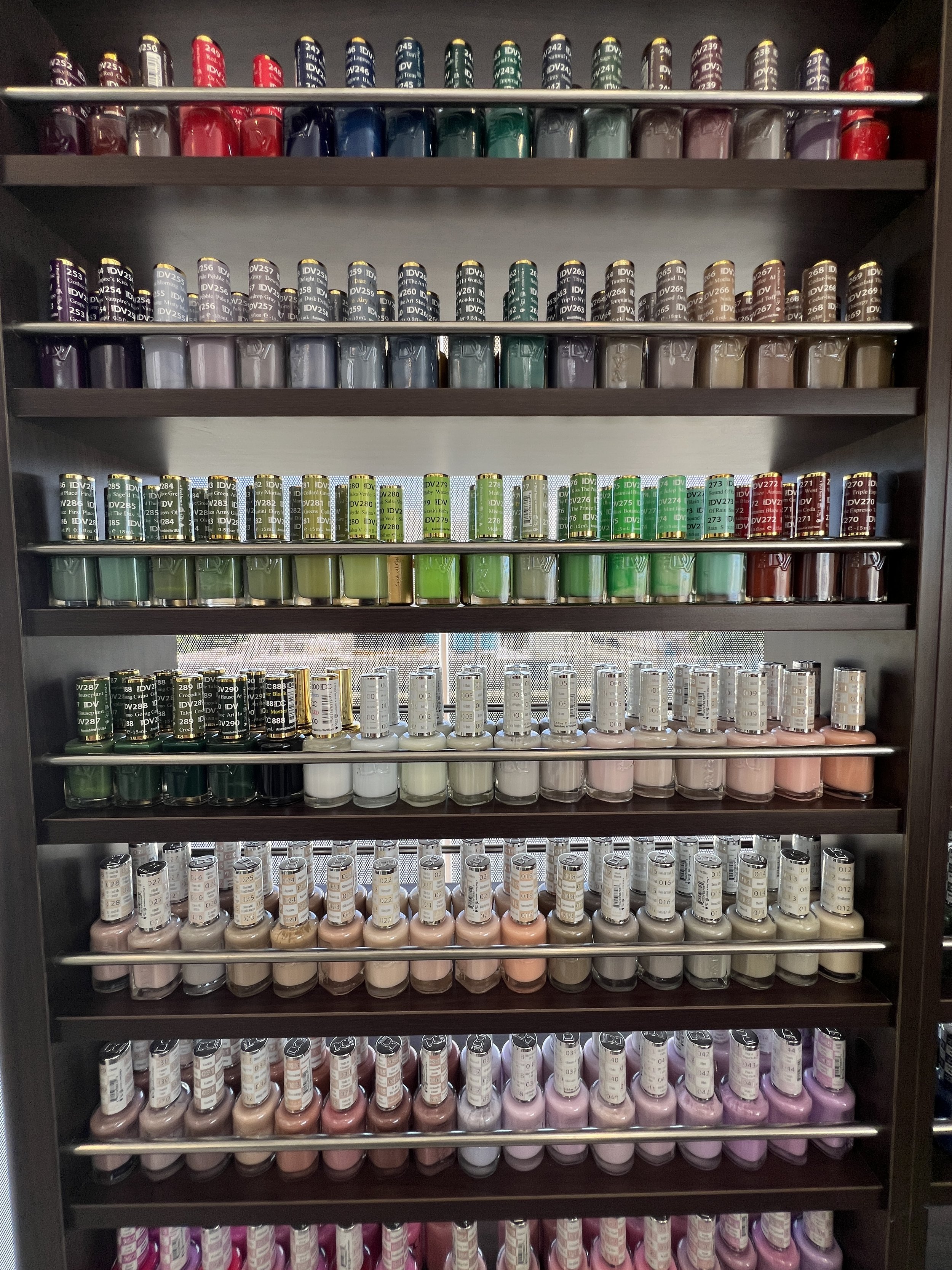 Estantería con varias filas de esmaltes de uñas en diferentes colores.