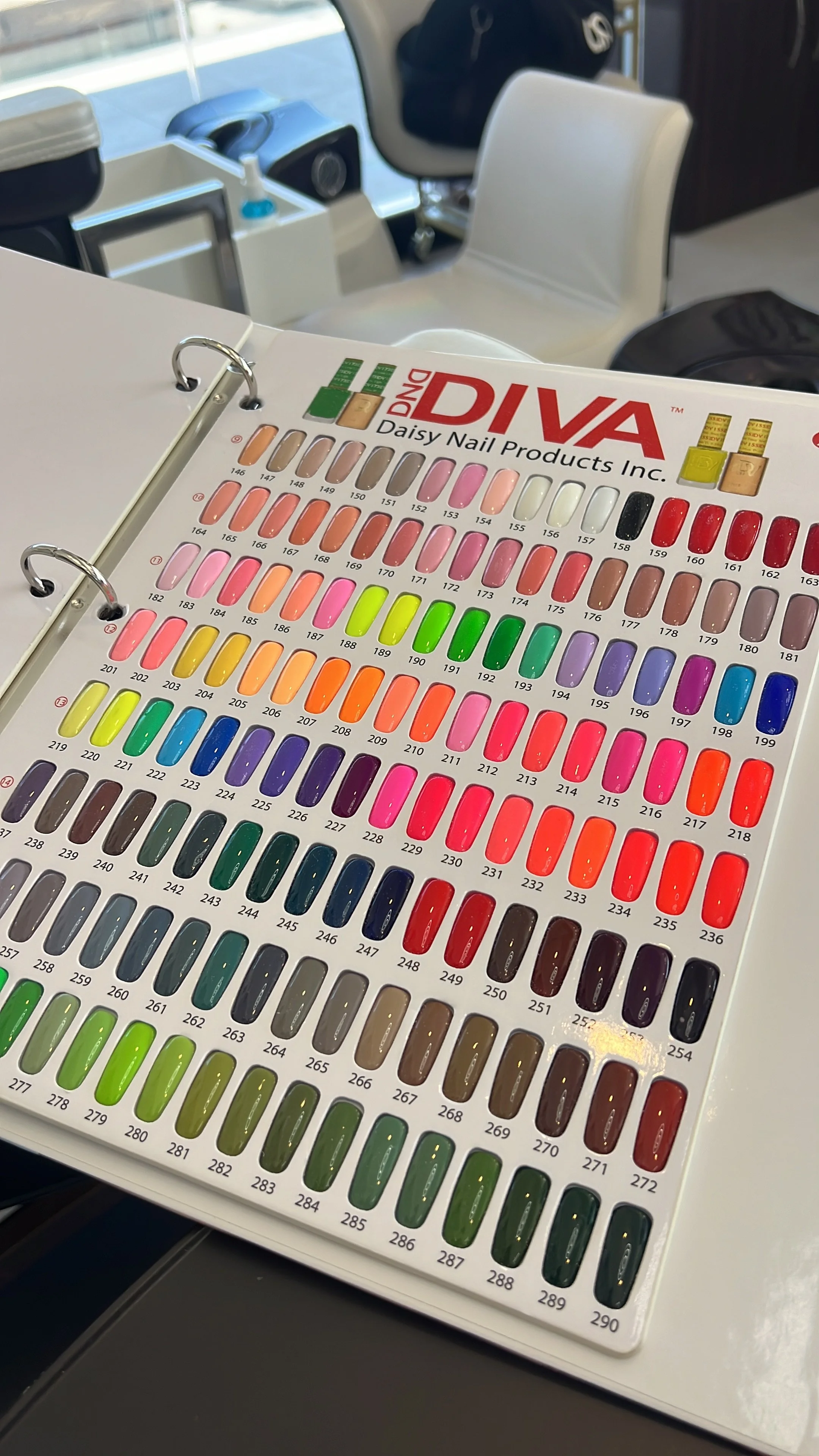 Muestrario de esmaltes de uñas con múltiples colores en una libreta con anillas. La libreta está sobre una mesa en un entorno de oficina o consultorio.