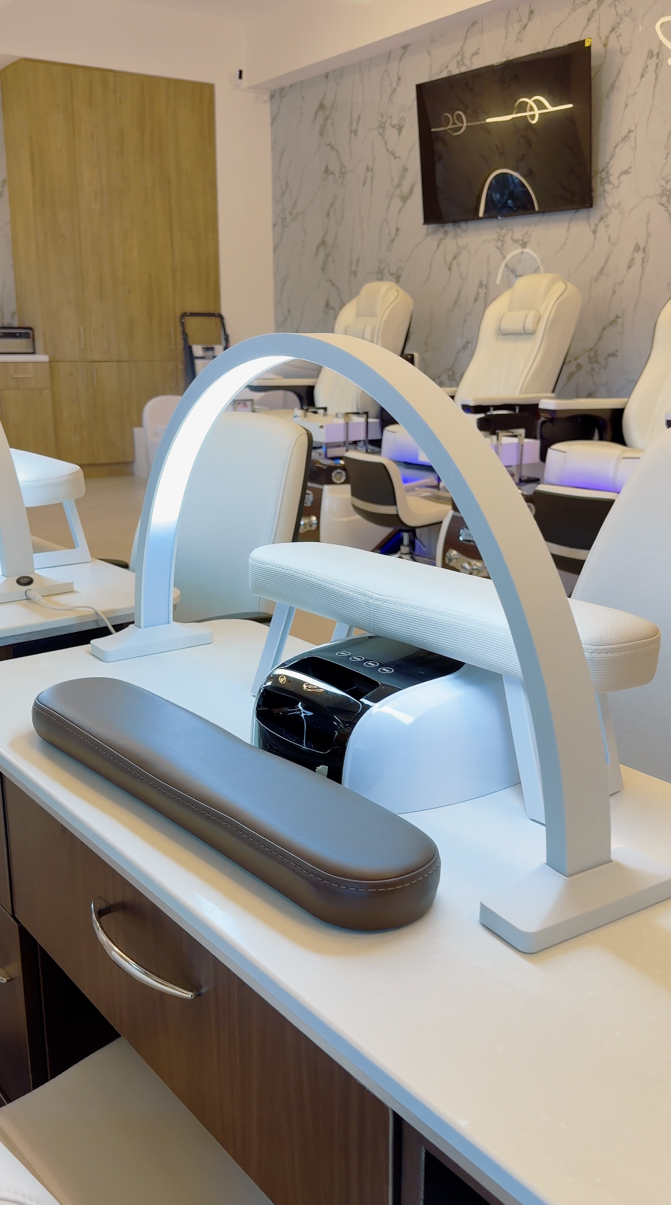 Equipo de manicura o cuidado de uñas en un salón de belleza. Dispositivo con luz, cojín y máquina en una mesa de trabajo, con sillas blancas en el fondo.