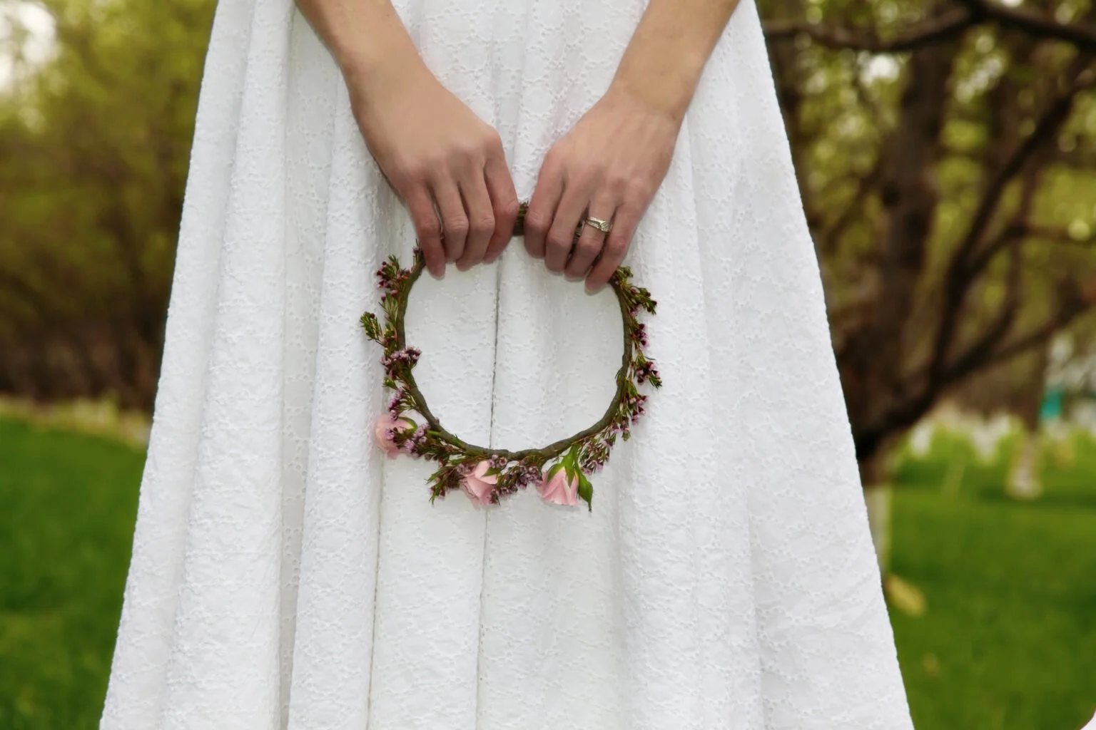hands hold flower crown in front of a white dress