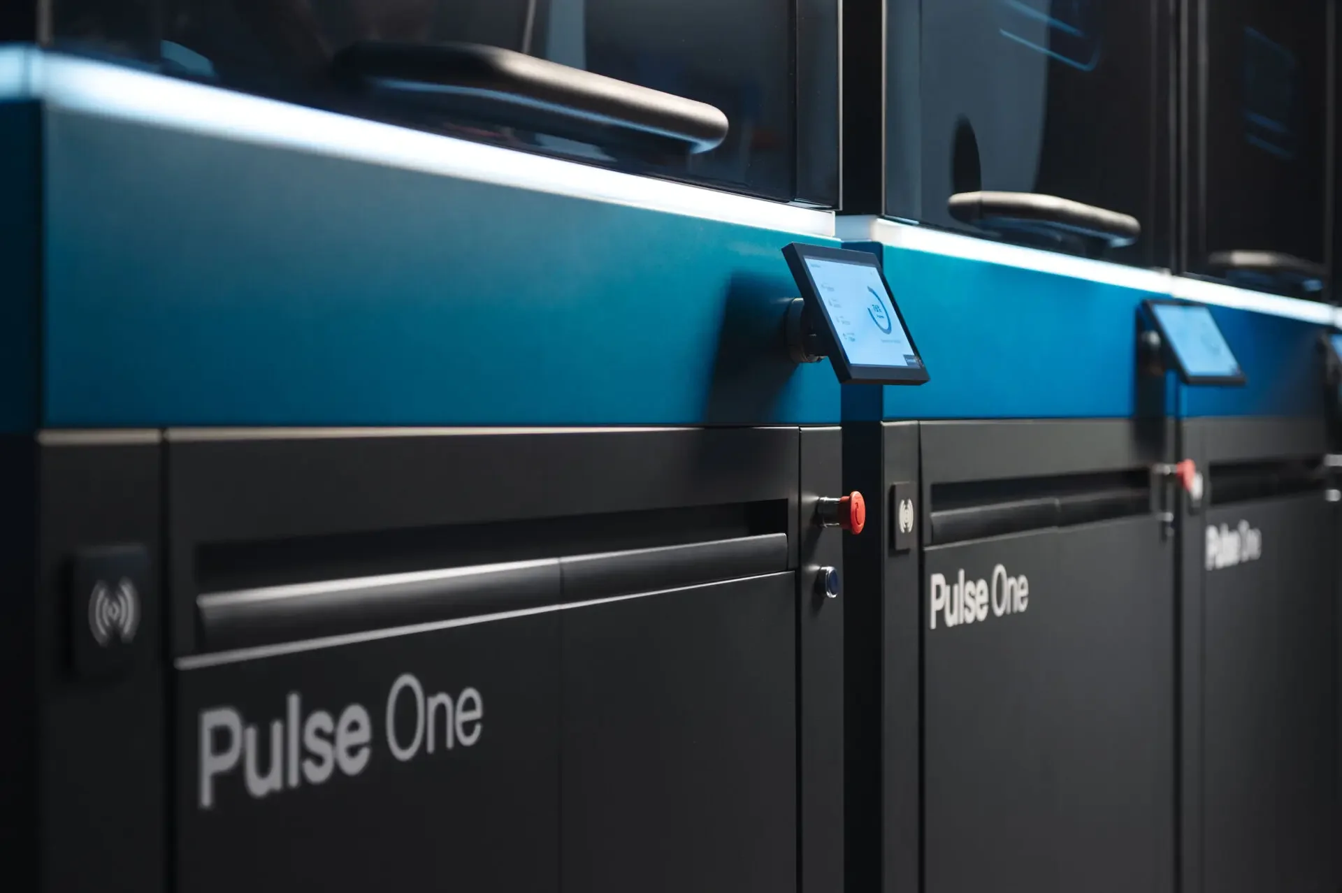Close-up of a black and blue industrial 3D printing machine labeled 'Pulse One', with digital screens and control buttons.