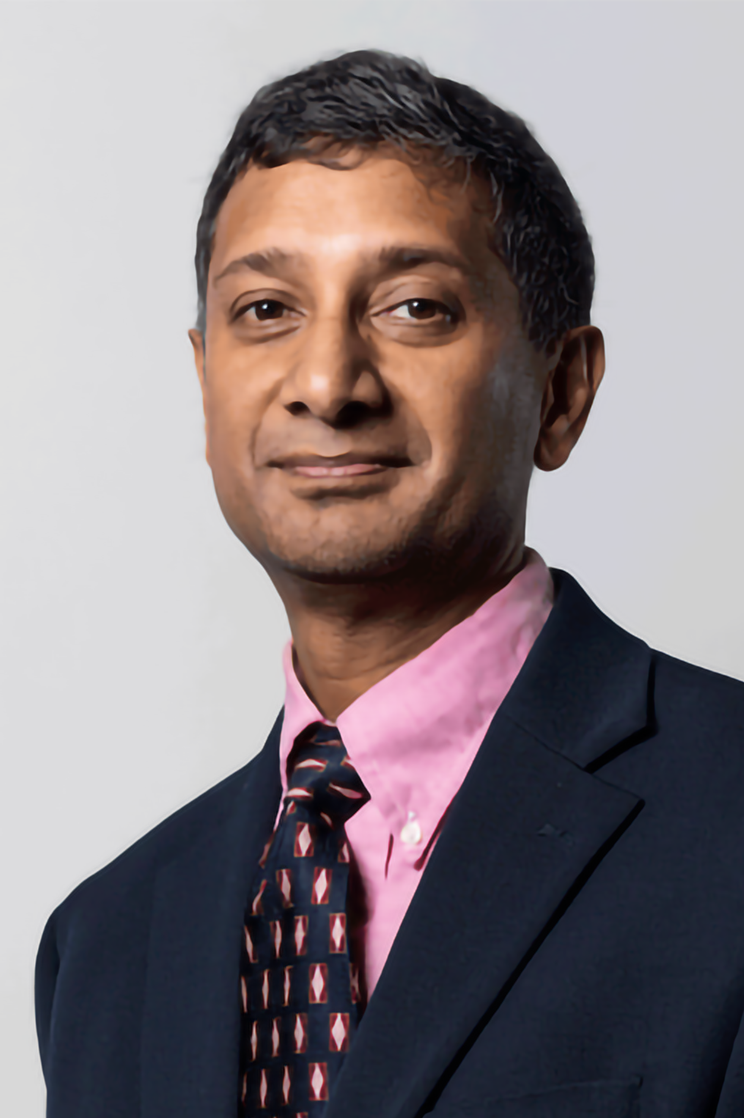 Portrait of a man in a suit with a pink shirt and a patterned tie, against a plain light background.
