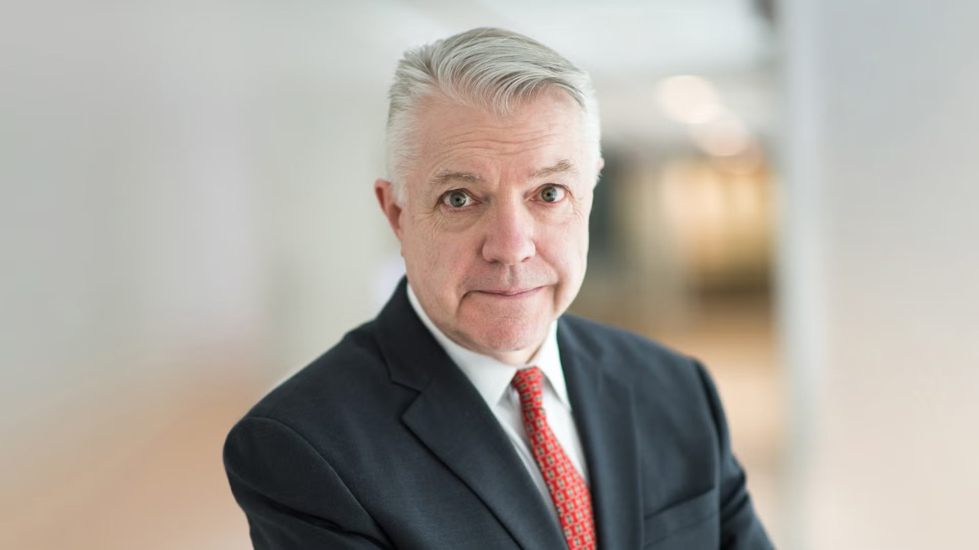 Portrait of a mature man with gray hair in a business suit and red tie, looking at the camera with a neutral expression, against a blurred background. Arthur Herman. 