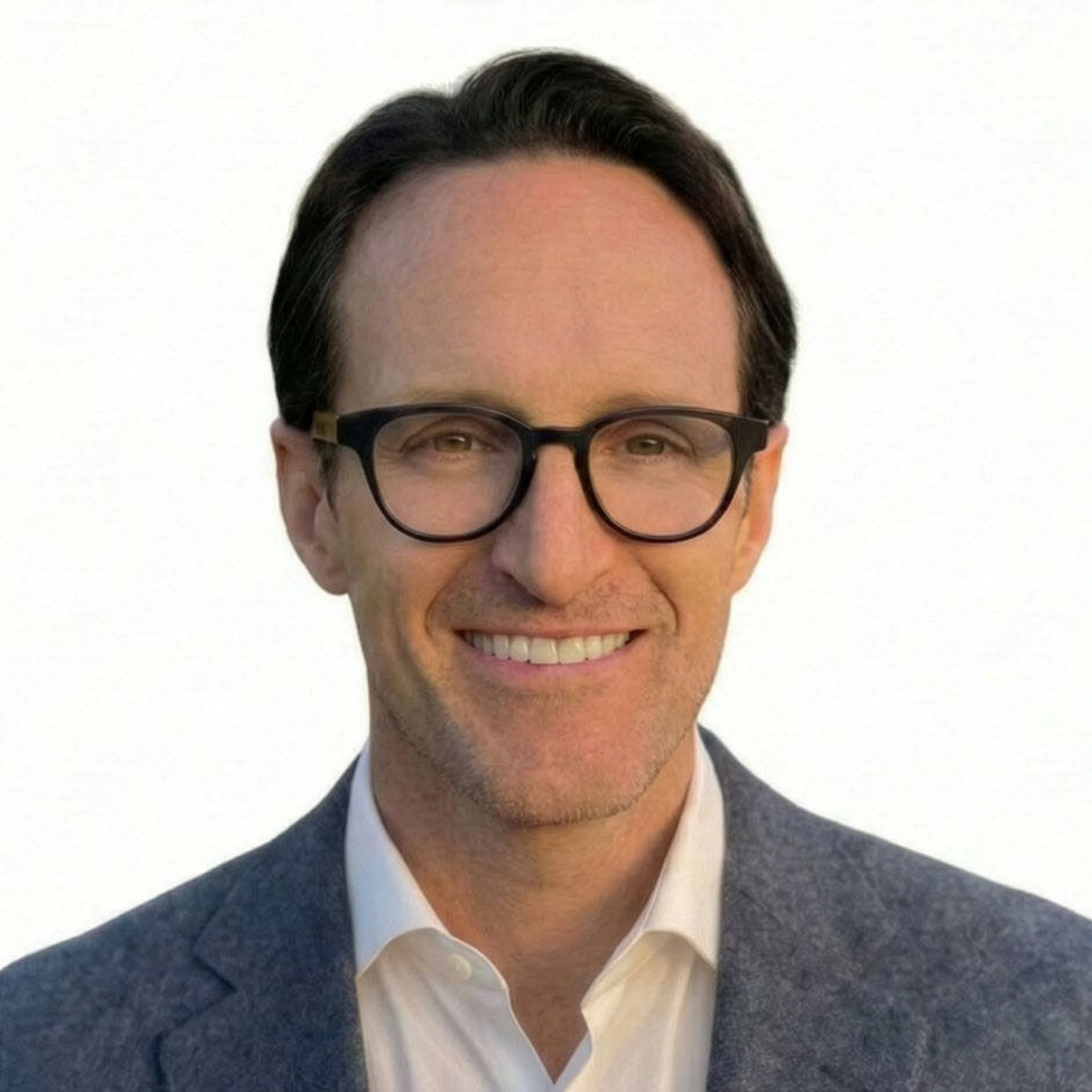 A man with dark hair, glasses, and a wide smile wearing a dark suit, white shirt, and tie, standing against a plain white background.