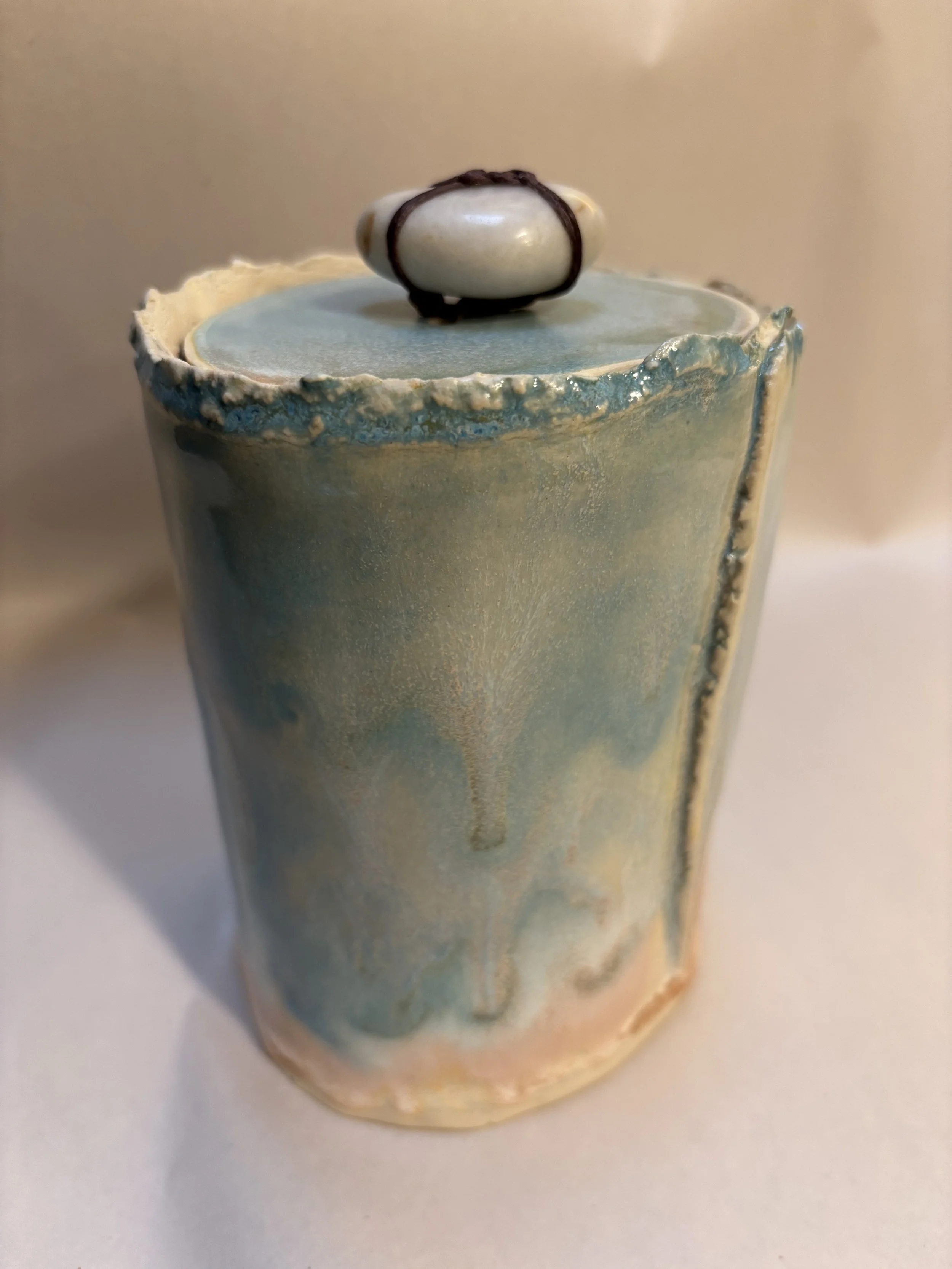 Close-up view of a blue and white ceramic cup with a gray interior, topped with a small white object tied with brown string.