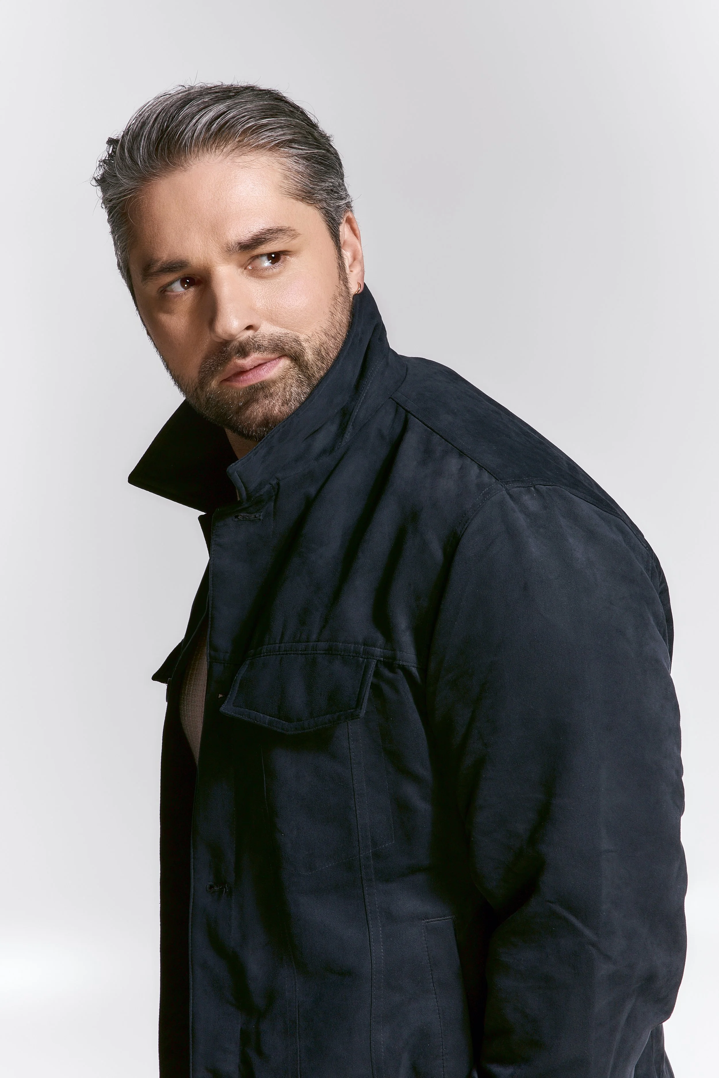 A man with short, gray hair and a beard, wearing a dark jacket, looking to his left against a plain white background.