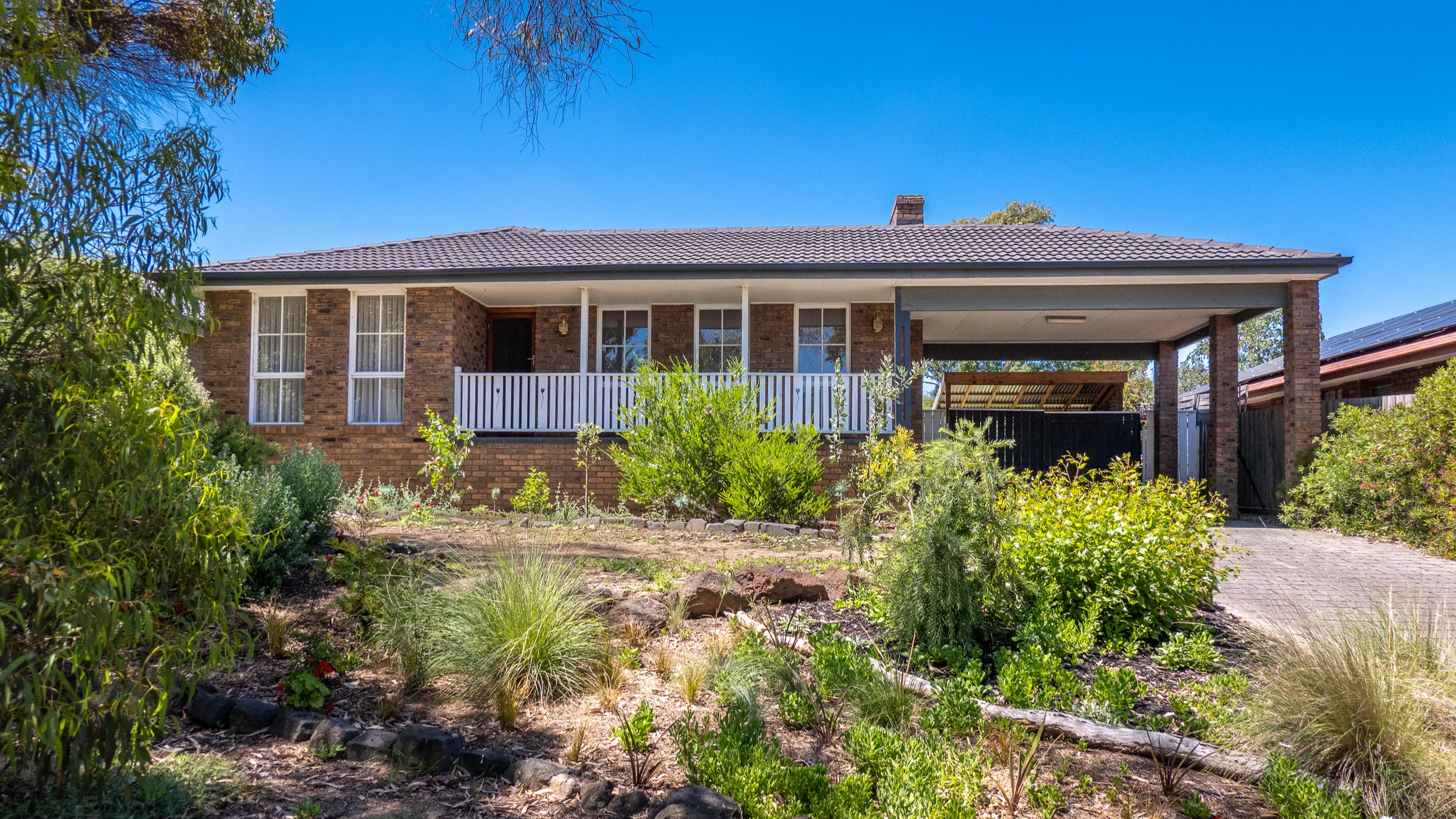 A brick house with a front yard garden and a covered porch, under a clear blue sky.