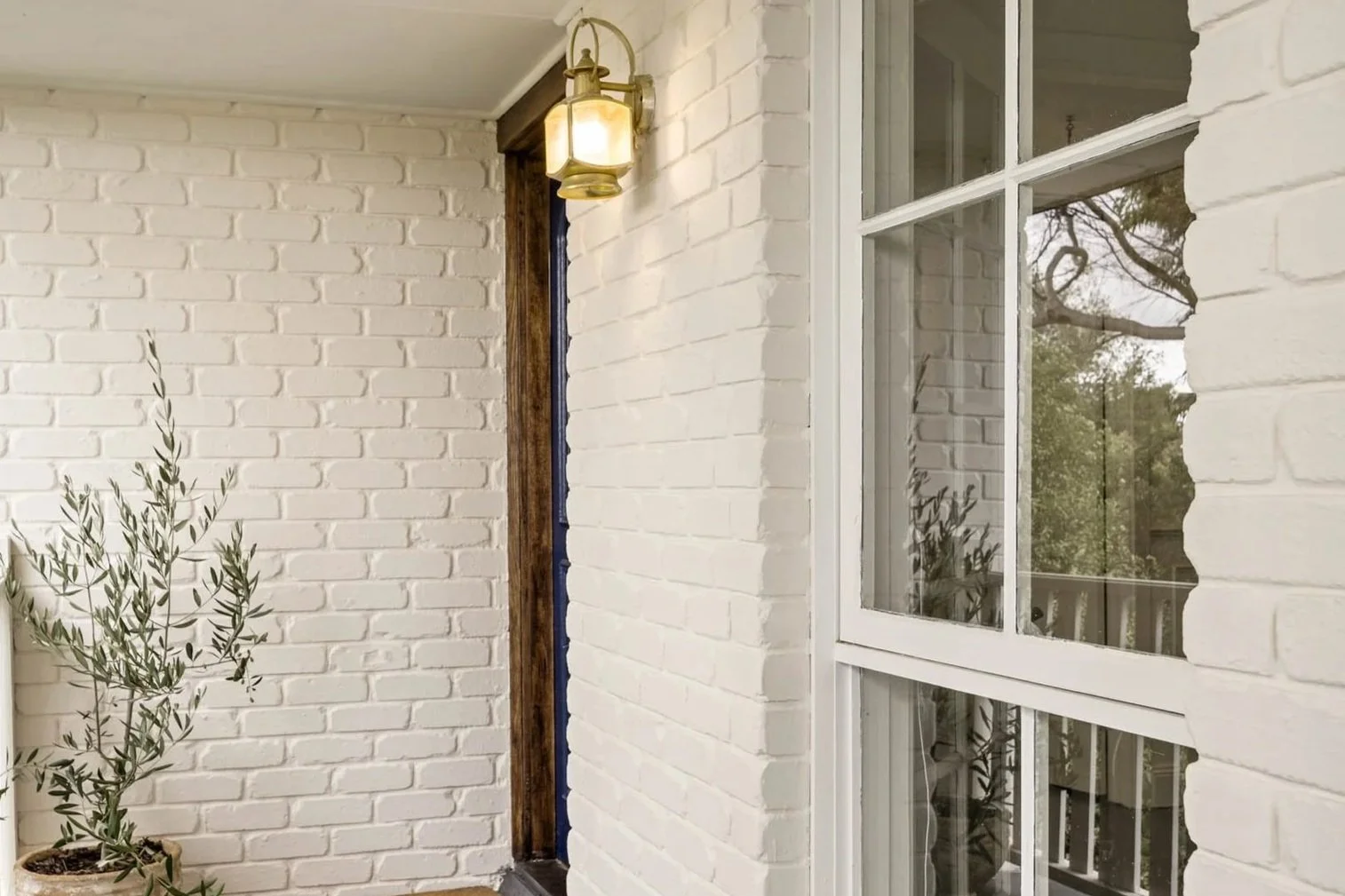Exterior corner of a house with limewashed brick walls, a large window, and a porch light.