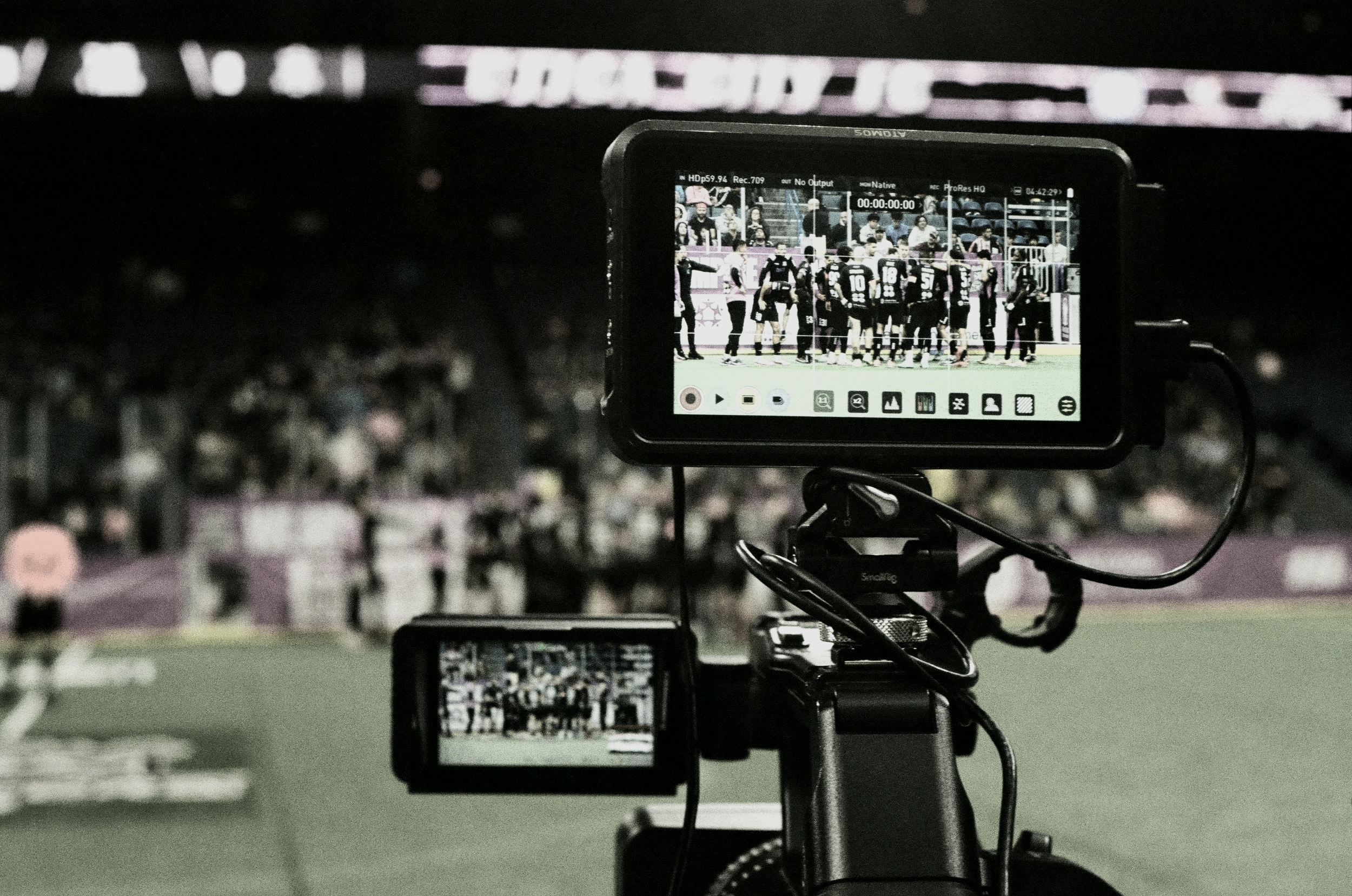 A video camera recording a sports event in an indoor stadium with a crowd in the background.