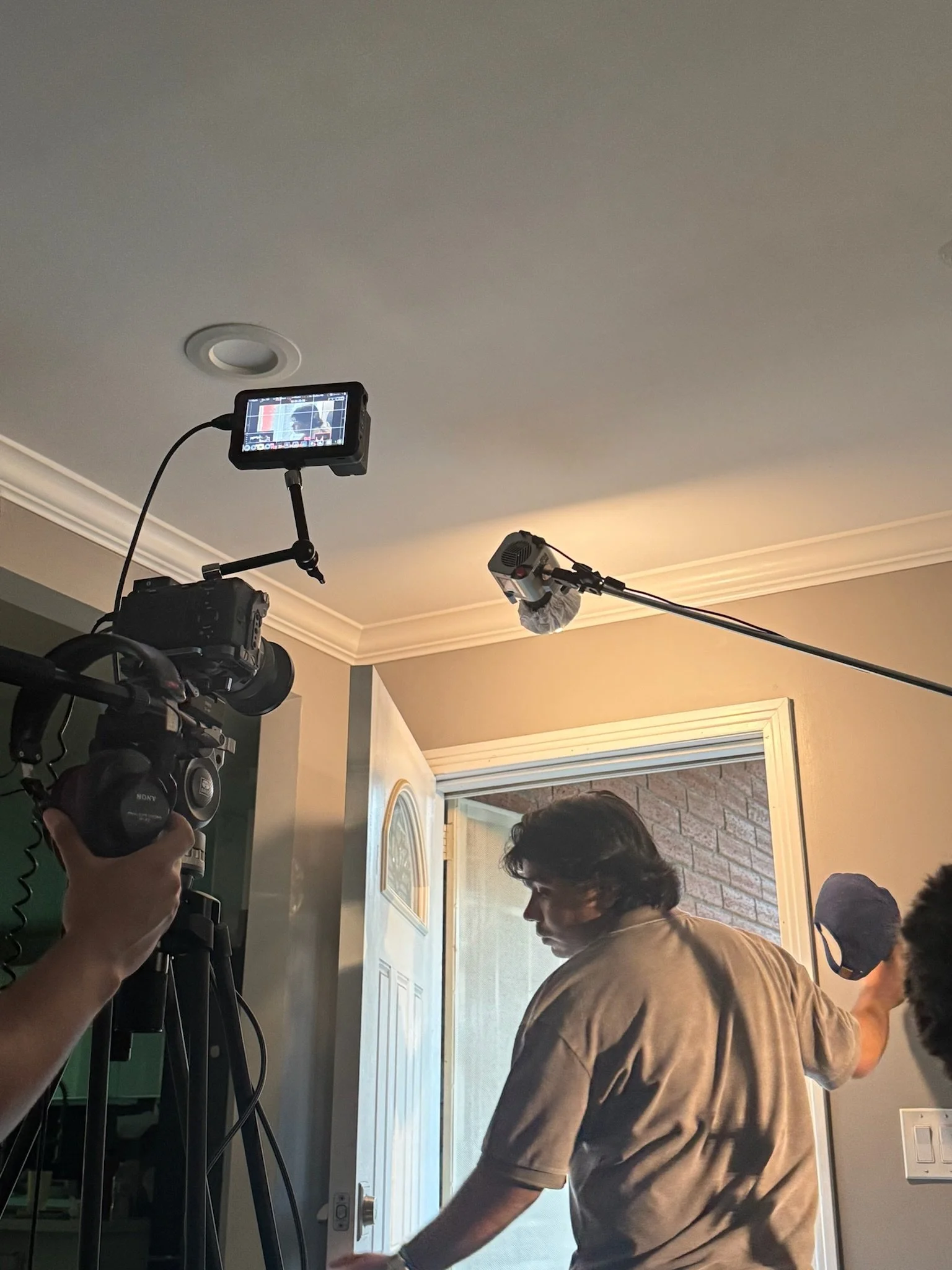 Filming scene with camera, monitor, and crew inside a home, with a man opening a door.
