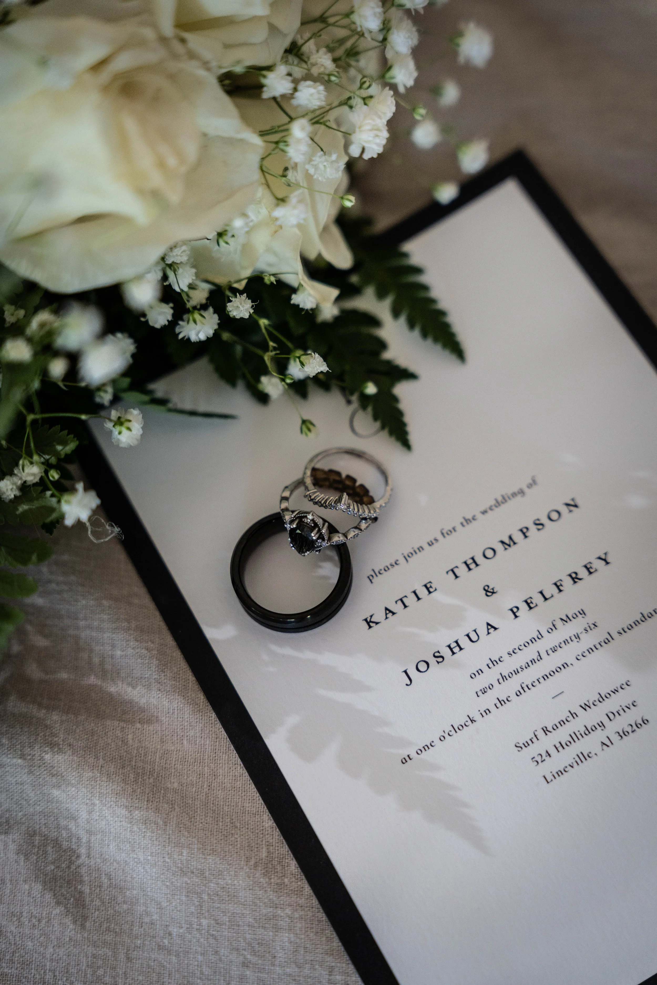 Wedding invitation card with wedding rings and white flowers on top.