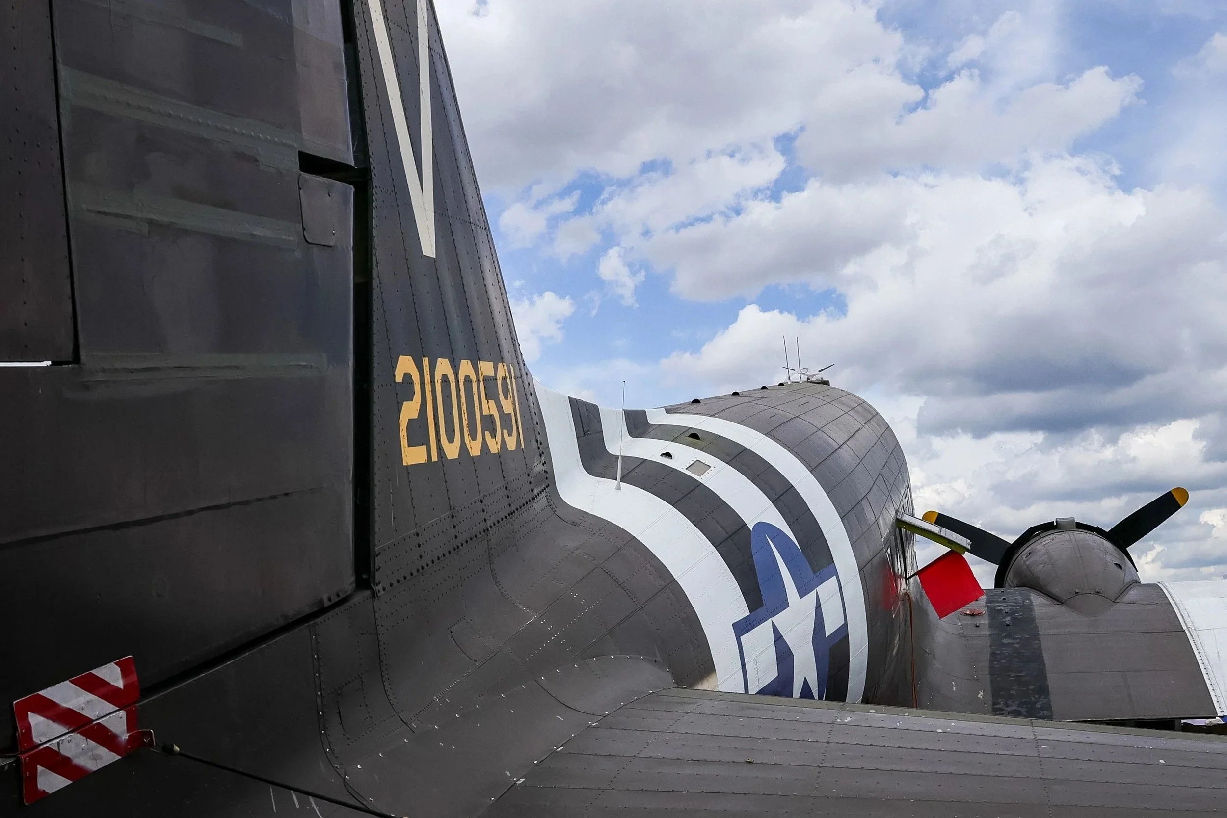 Close-up side view of a military jet aircraft with black and white markings, yellow identification number, and gray clouds sky background.