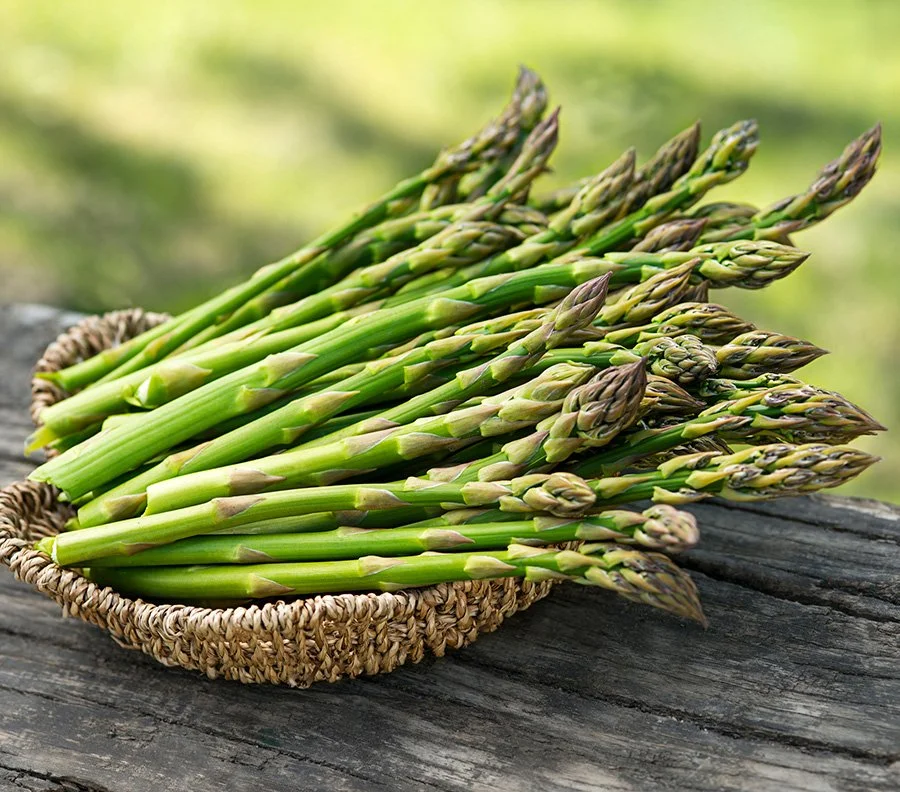 Fresh asparagus spears in a woven basket on a wooden surface outdoors