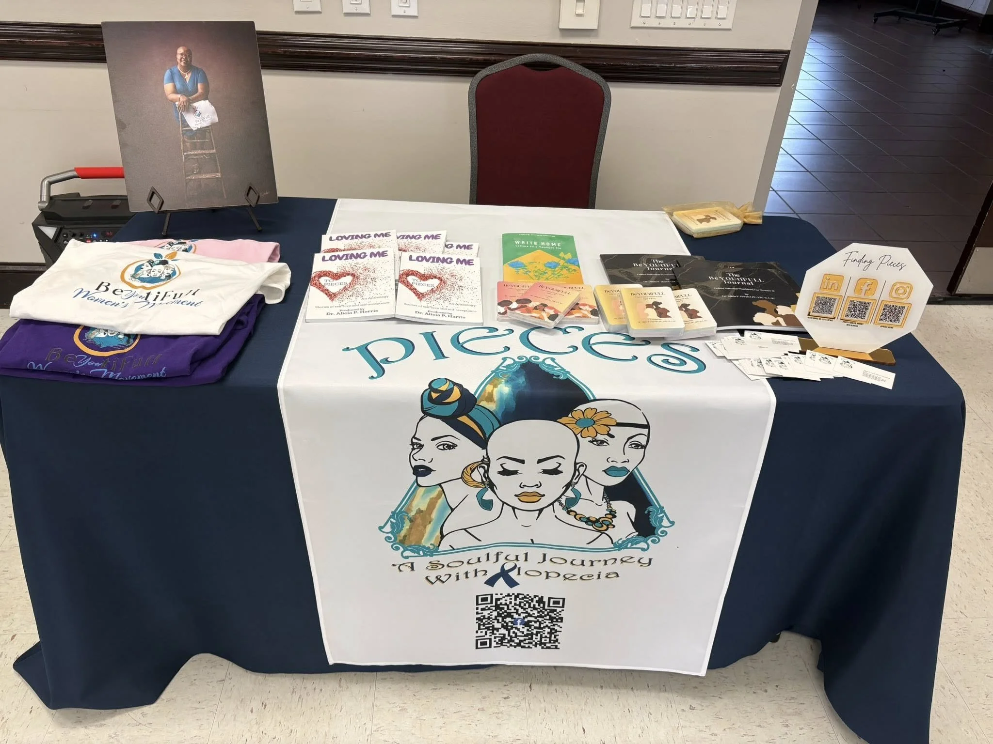 A table with promotional materials including brochures, flyers, tote bags, and QR code cards related to a faith-based initiative called "A Soulful Journey with Xplorea." The table displays a large illustration of three diverse women with their eyes closed and serene expressions, with hair styled and adorned with flowers and jewelry.