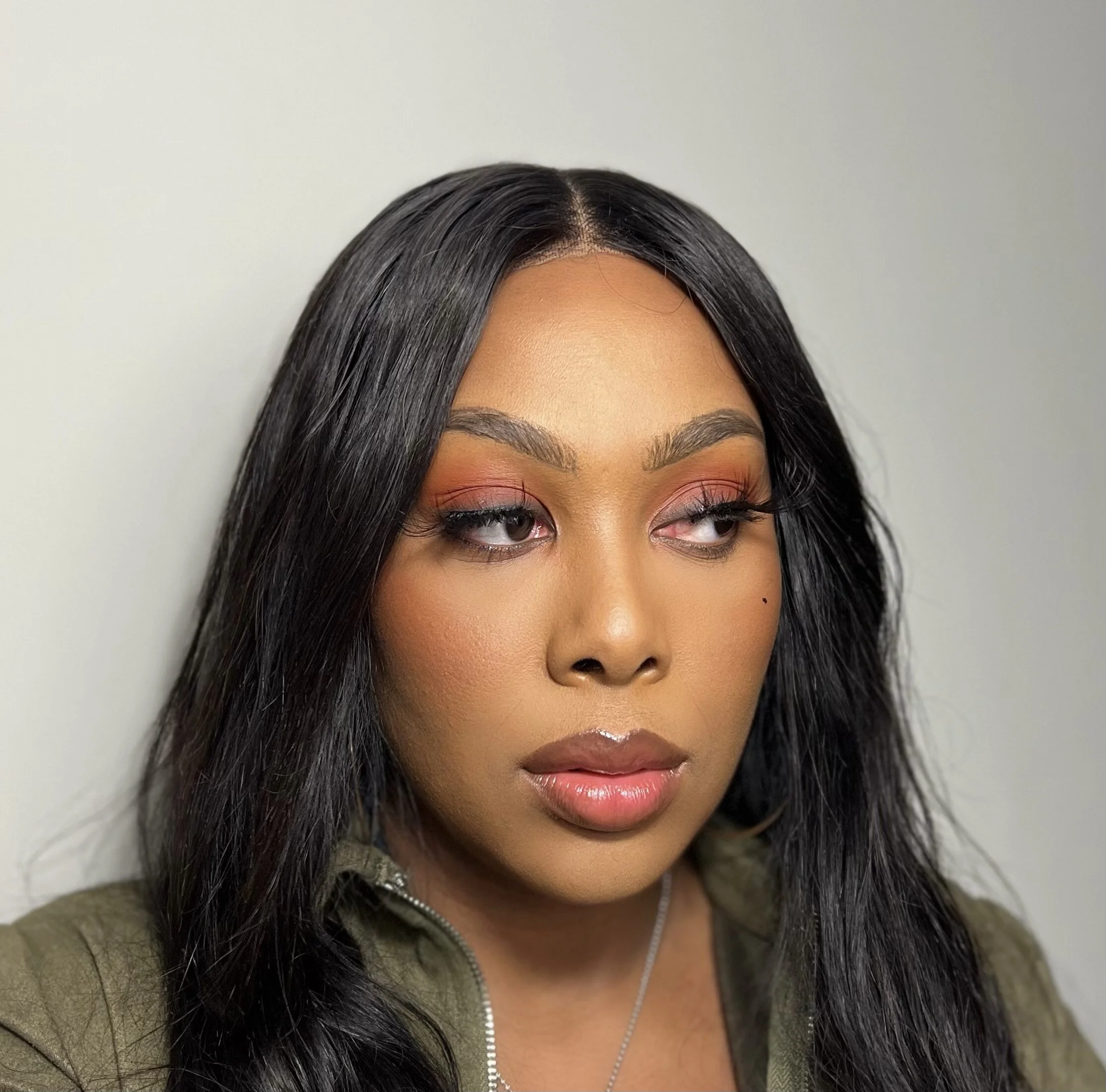 Close-up of a woman's face with long black hair, wearing makeup with pink eyeshadow, and a green jacket with a zipper.