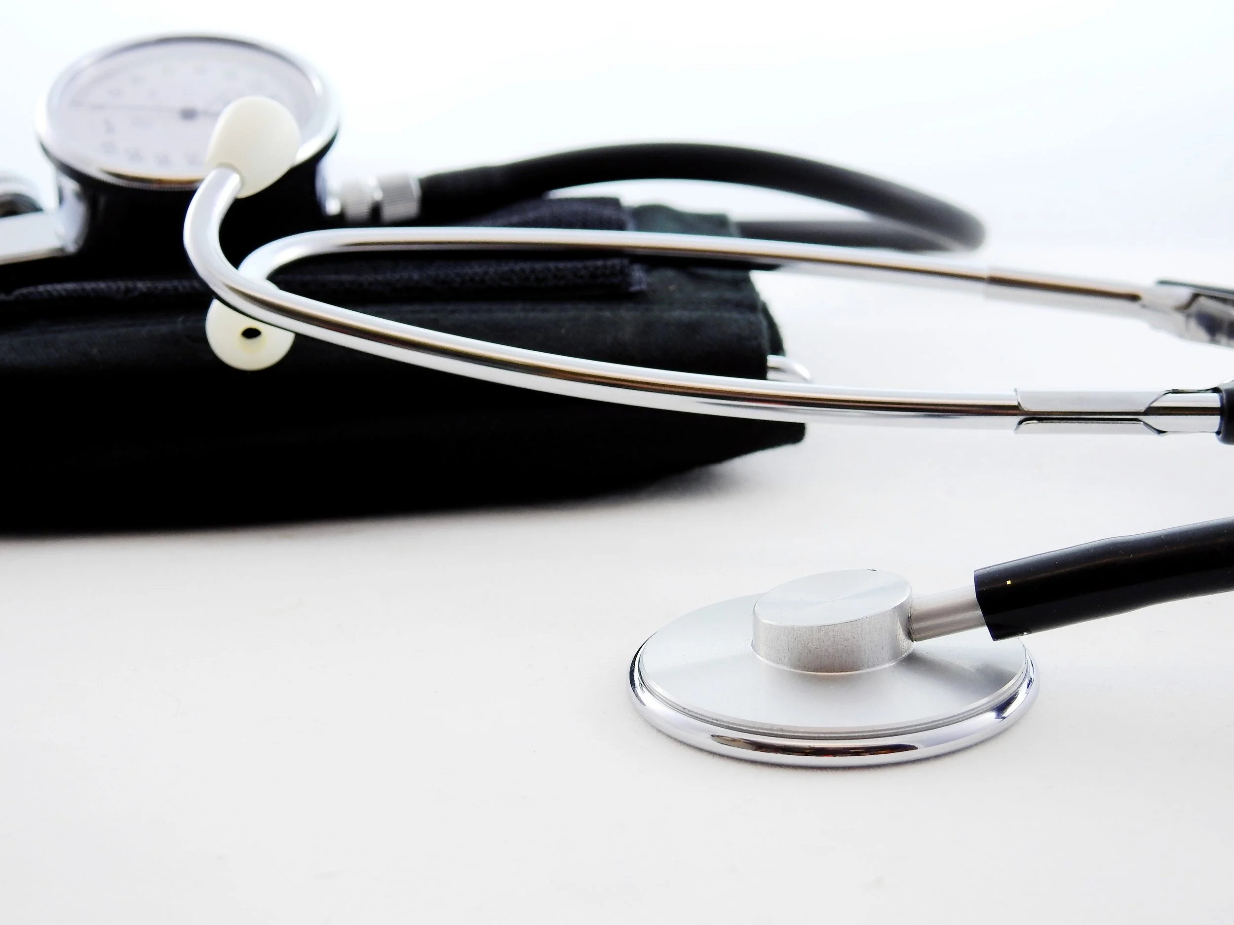 Close-up of a stethoscope placed on a black surface, with its silver chest piece and white tubing visible, and a white pen on a white surface.