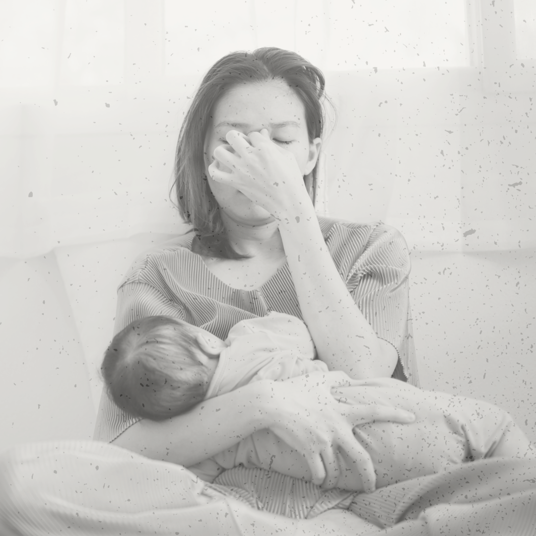 A woman holding a newborn baby in her arms, with her hand covering her face, sitting in a hospital setting.