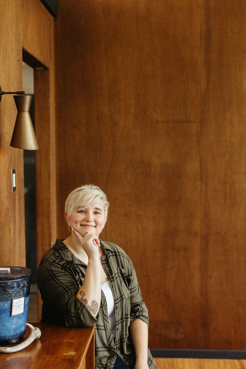 Lauren Abbott, sitting at a wooden table with her chin resting on her hand, inside a room with wood-paneled walls.