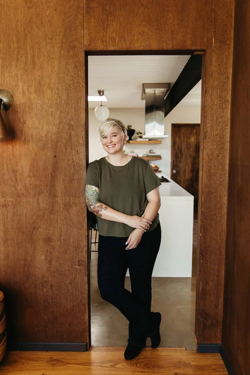 Lauren Abbott with tattoo sleeve on her left arm standing in a doorway, smiling at the camera.