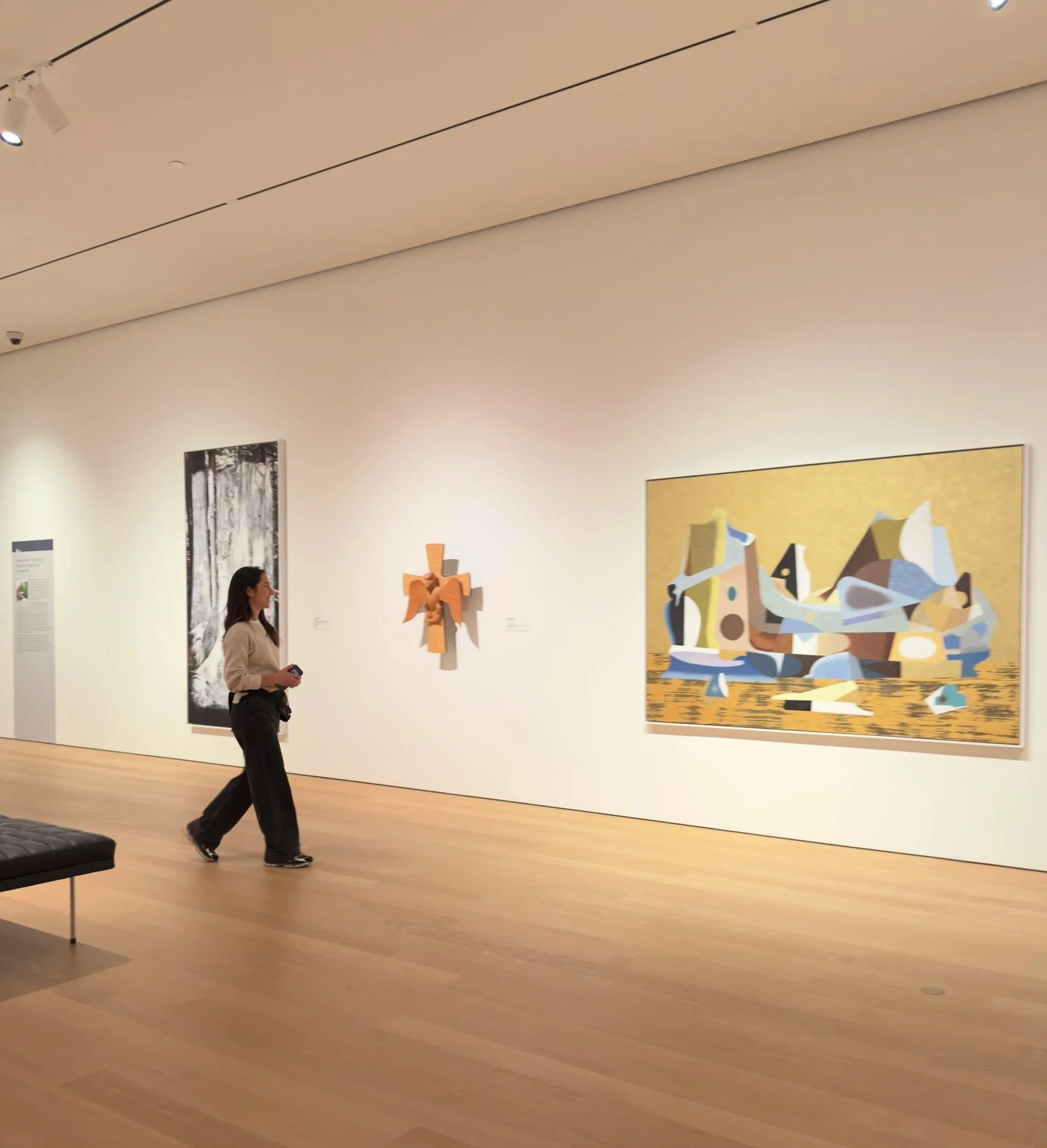 Woman walking in art gallery with abstract paintings on white walls and wooden floor.
