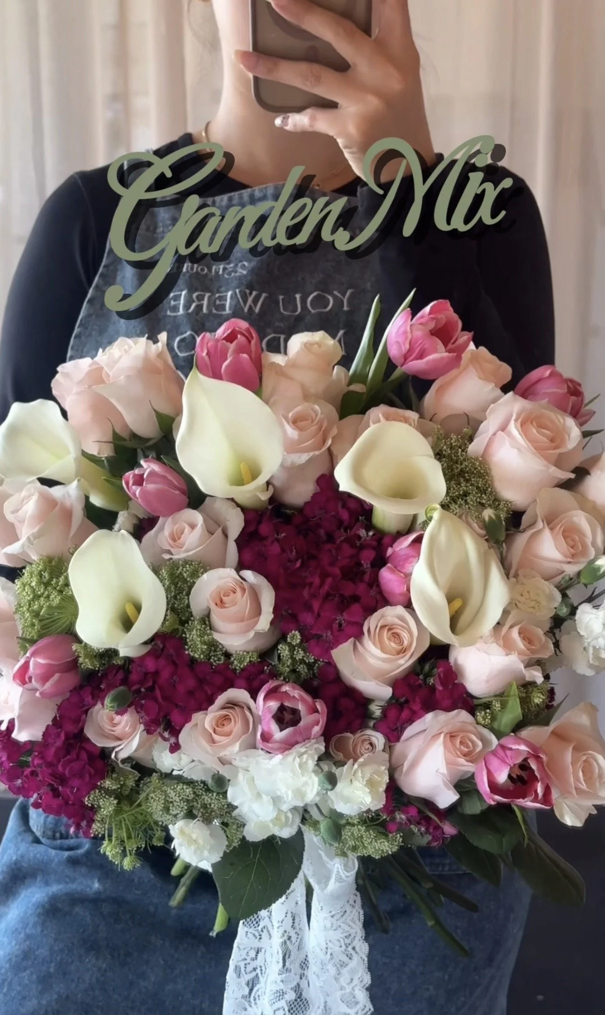 Person holding a large bouquet of pink, white, and cream flowers, including roses and calla lilies, with a lace ribbon around the bouquet.