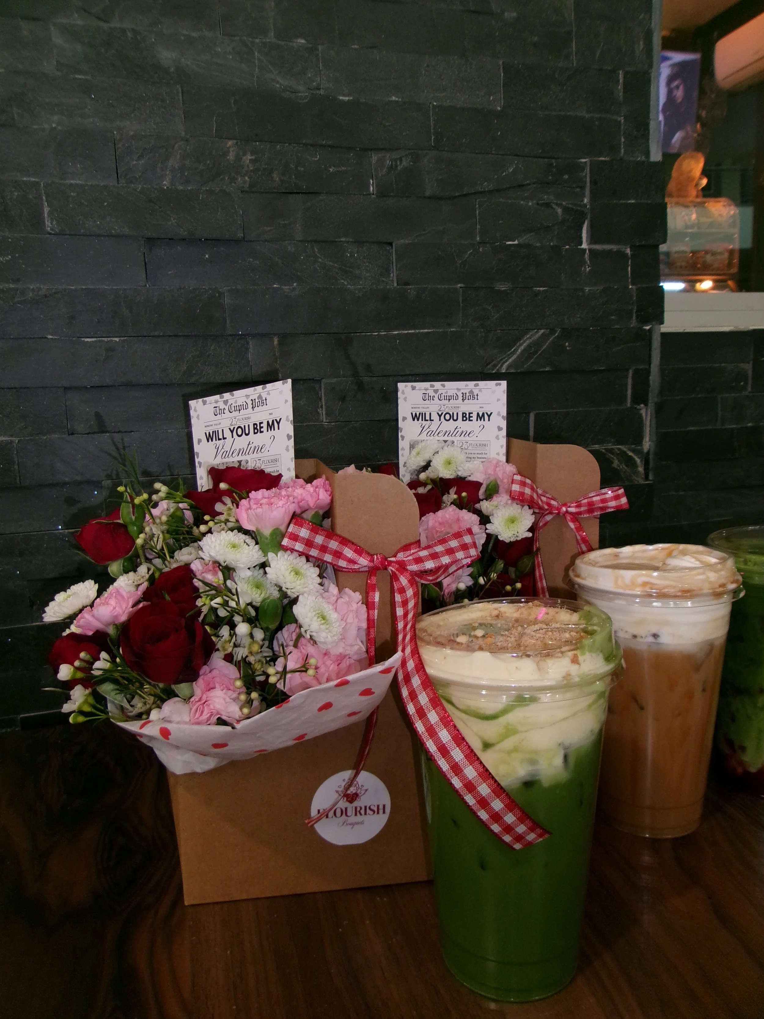 Flowers arranged in a bouquet with Valentine's Day cards and drinks on a table.