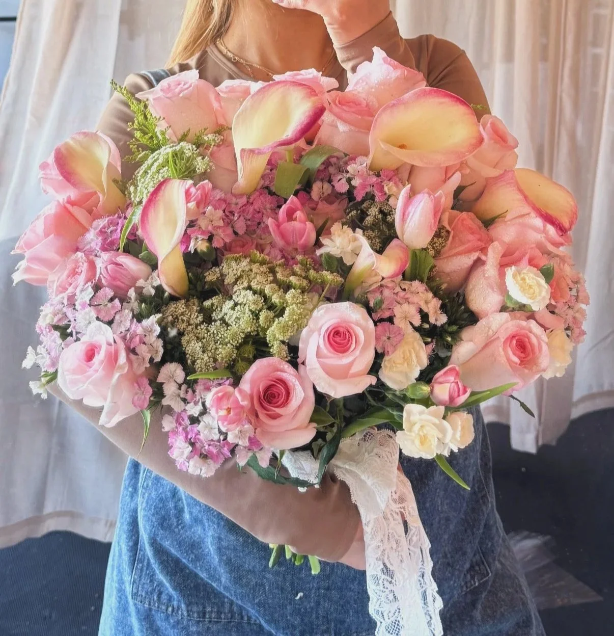Person holding a large bouquet of pink and cream roses, calla lilies, and other pink flowers.