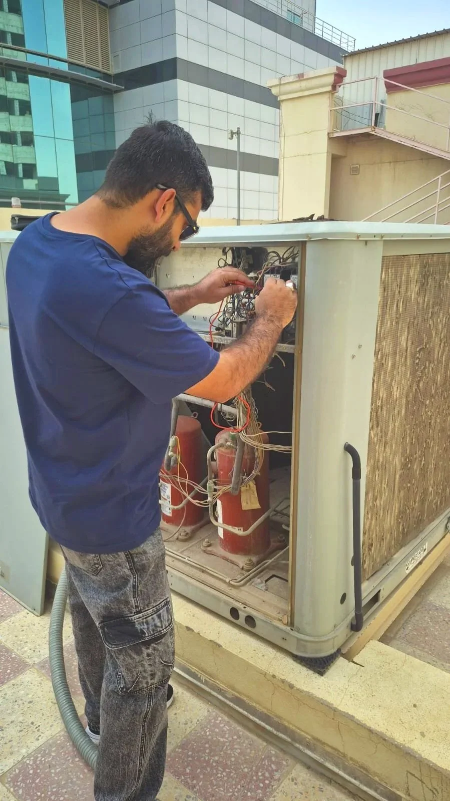 A technician repairing an outdoor HVAC unit with wires and components exposed.