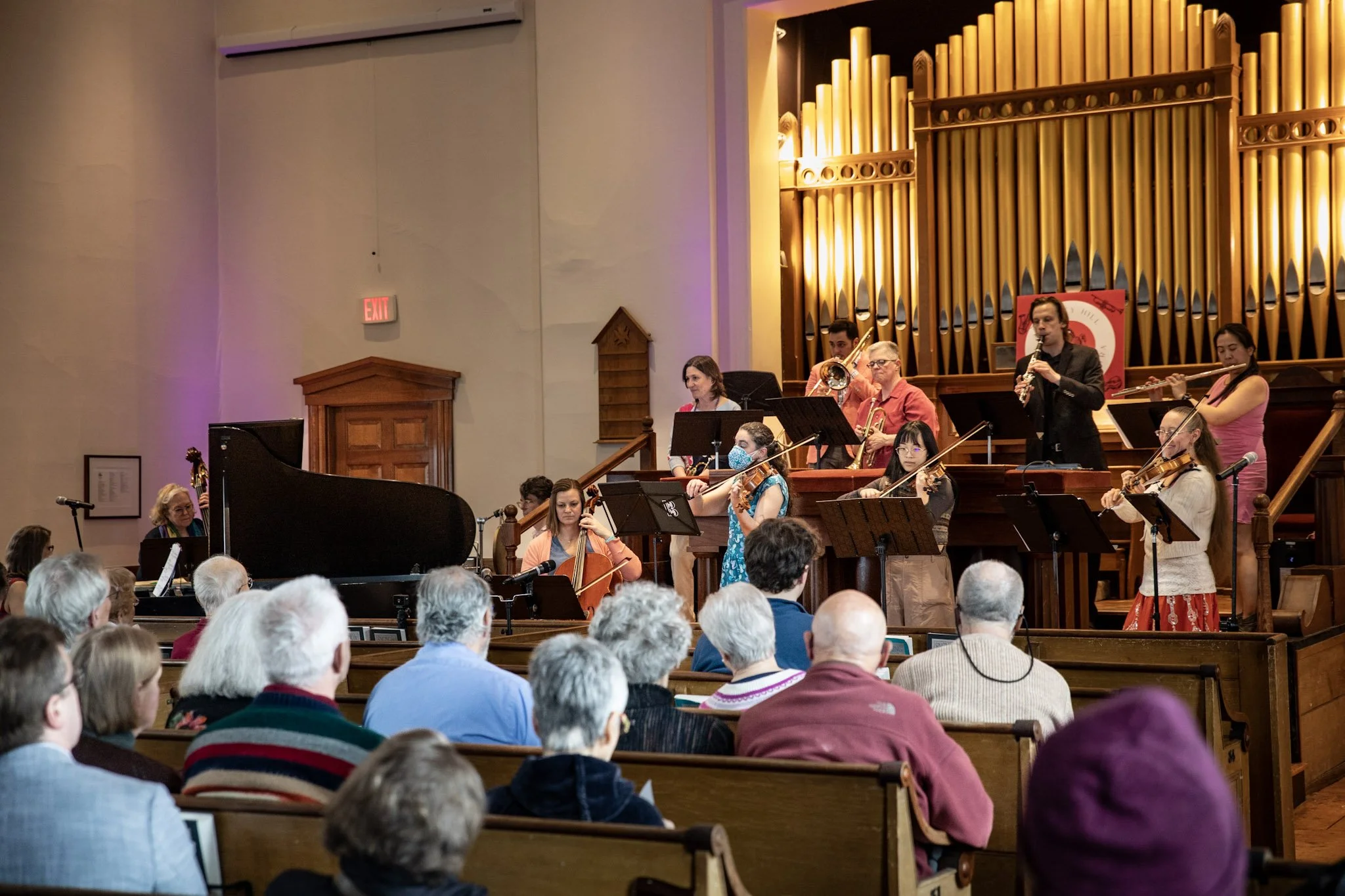 An orchestra performing in a church or concert hall with audience members watching.