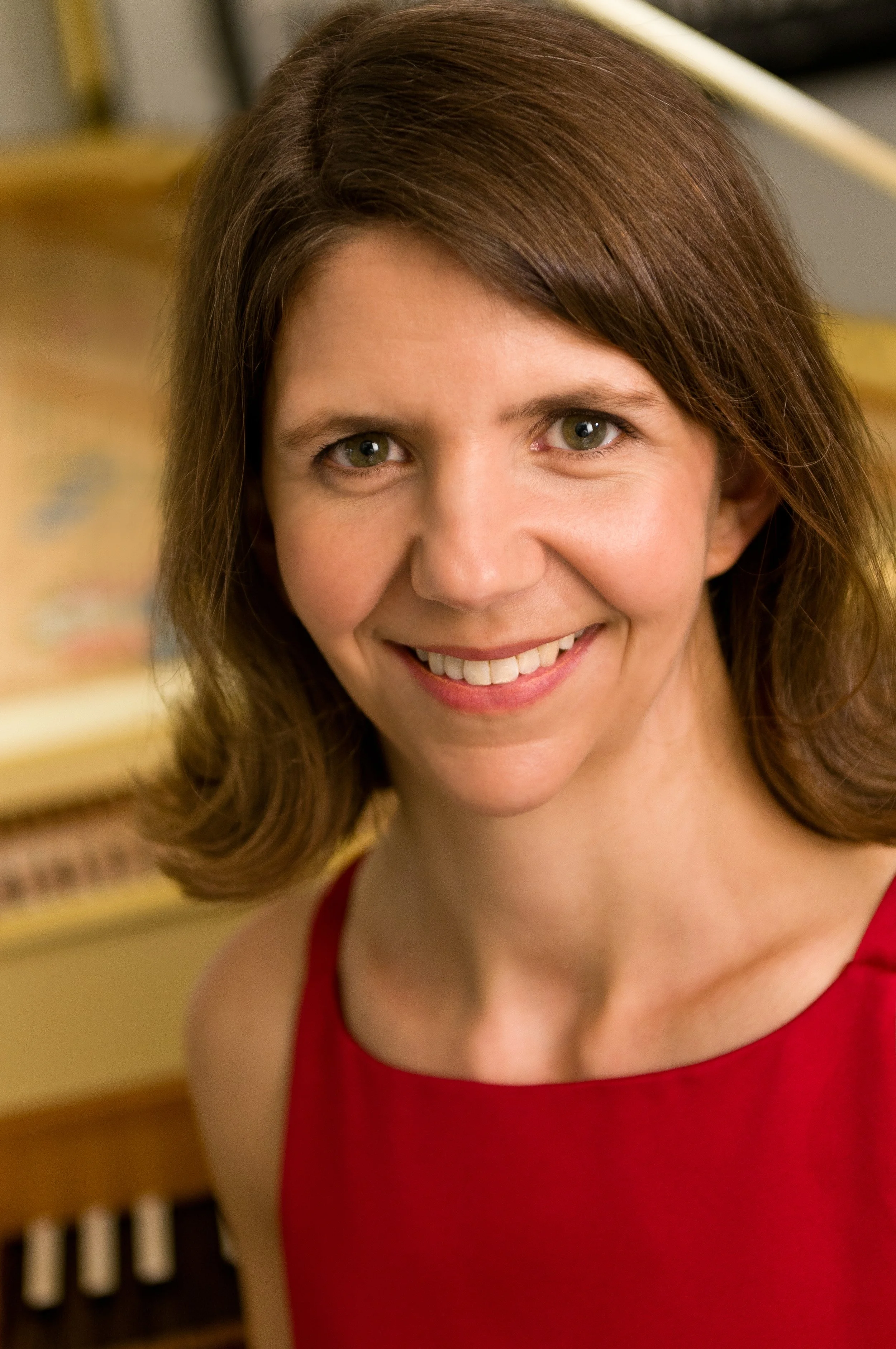 Close-up of a woman's face smiling, wearing a red top, with a background that appears to be a keyboard or musical instrument.