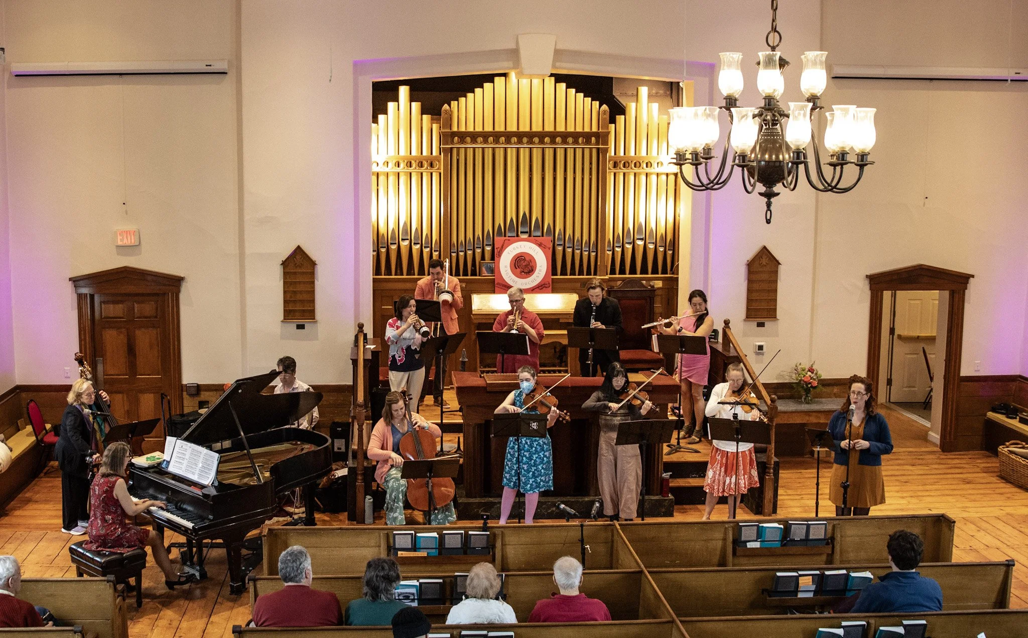 Orchestra performing in a concert hall with a large pipe organ in the background.