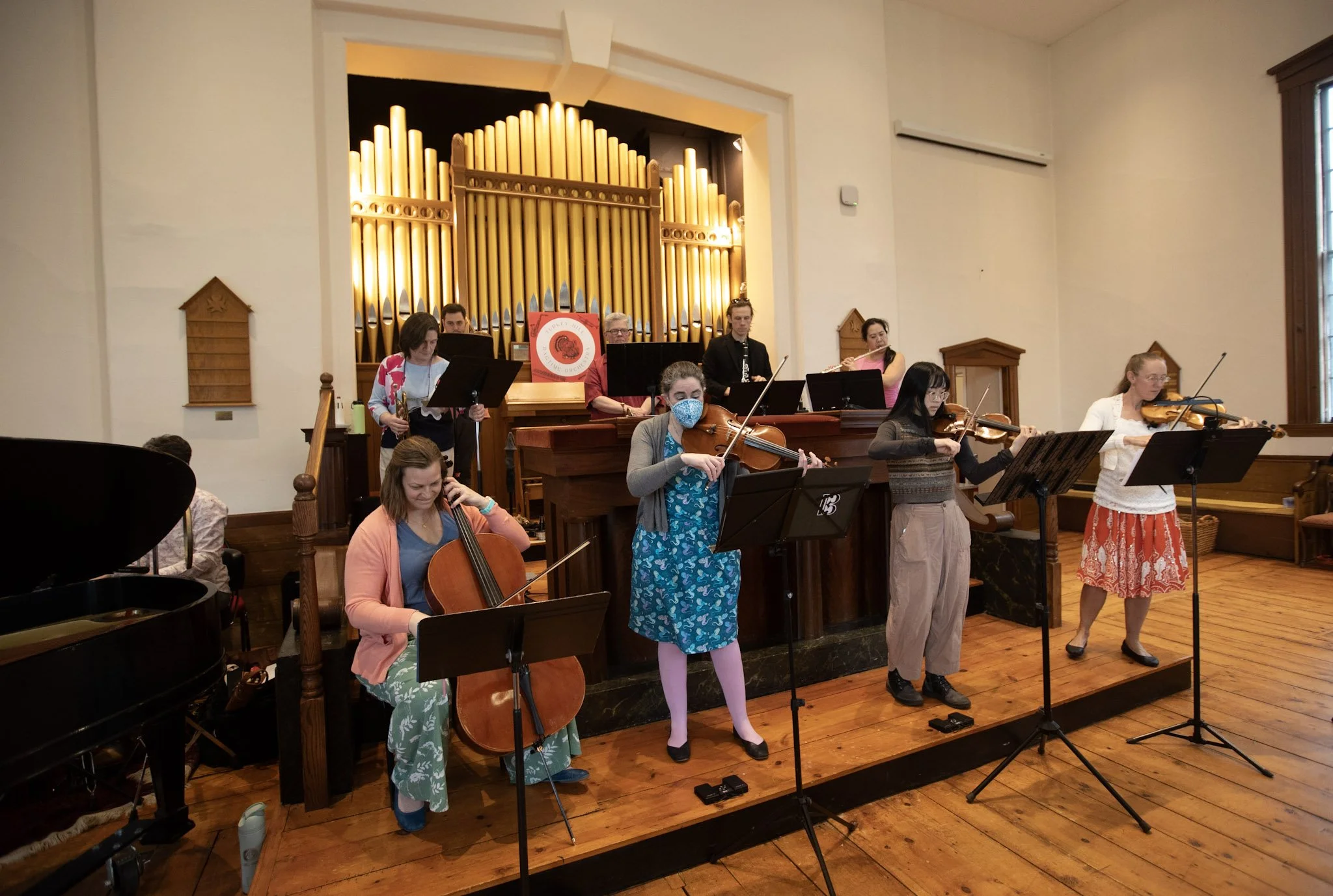 Orchestra rehearsal with musicians playing instruments such as the viola, violin, and double bass in a room with a large pipe organ in the background.