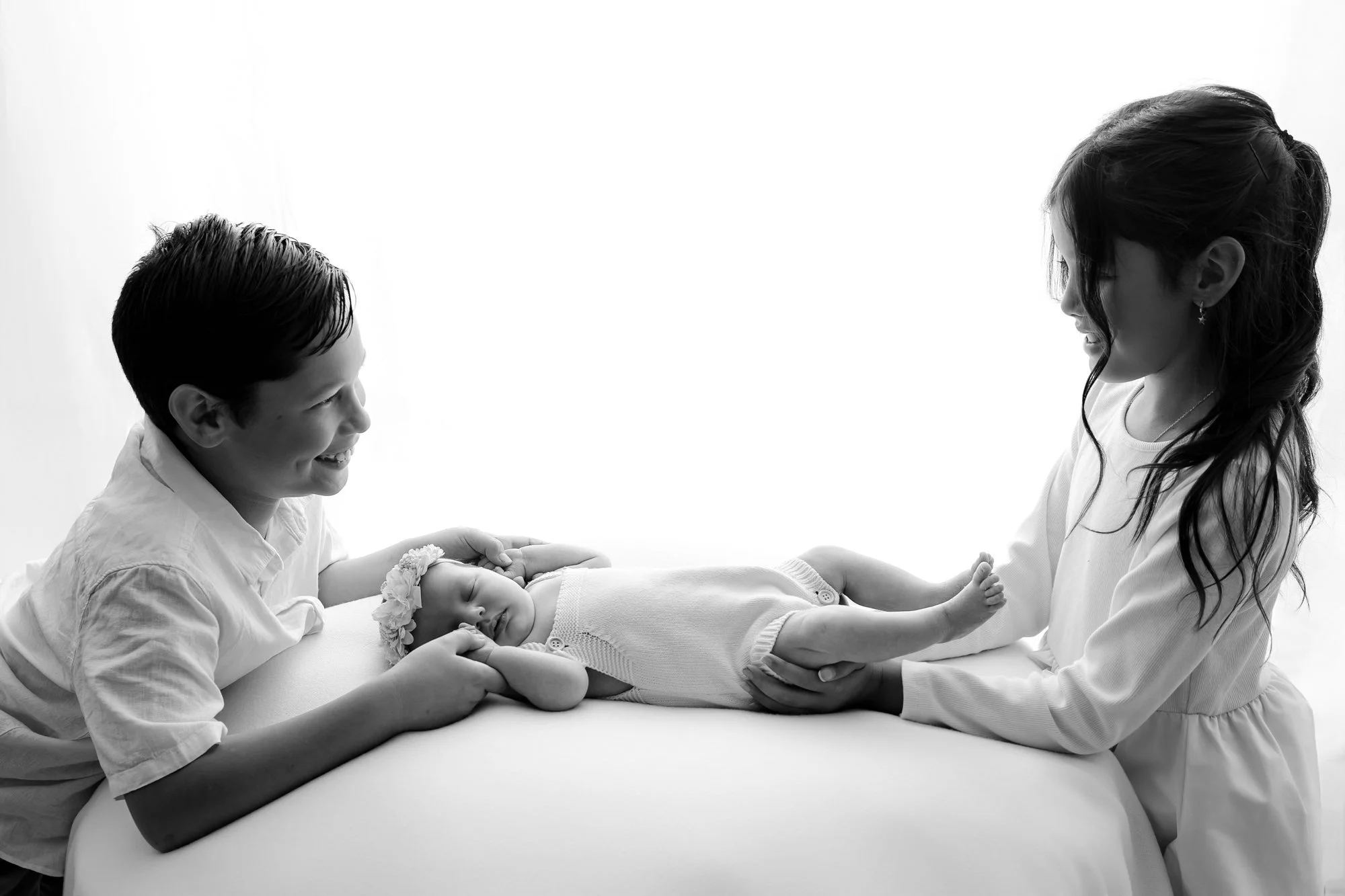 Big siblings leaning over their new baby sister at their family newborn photography session in Melton