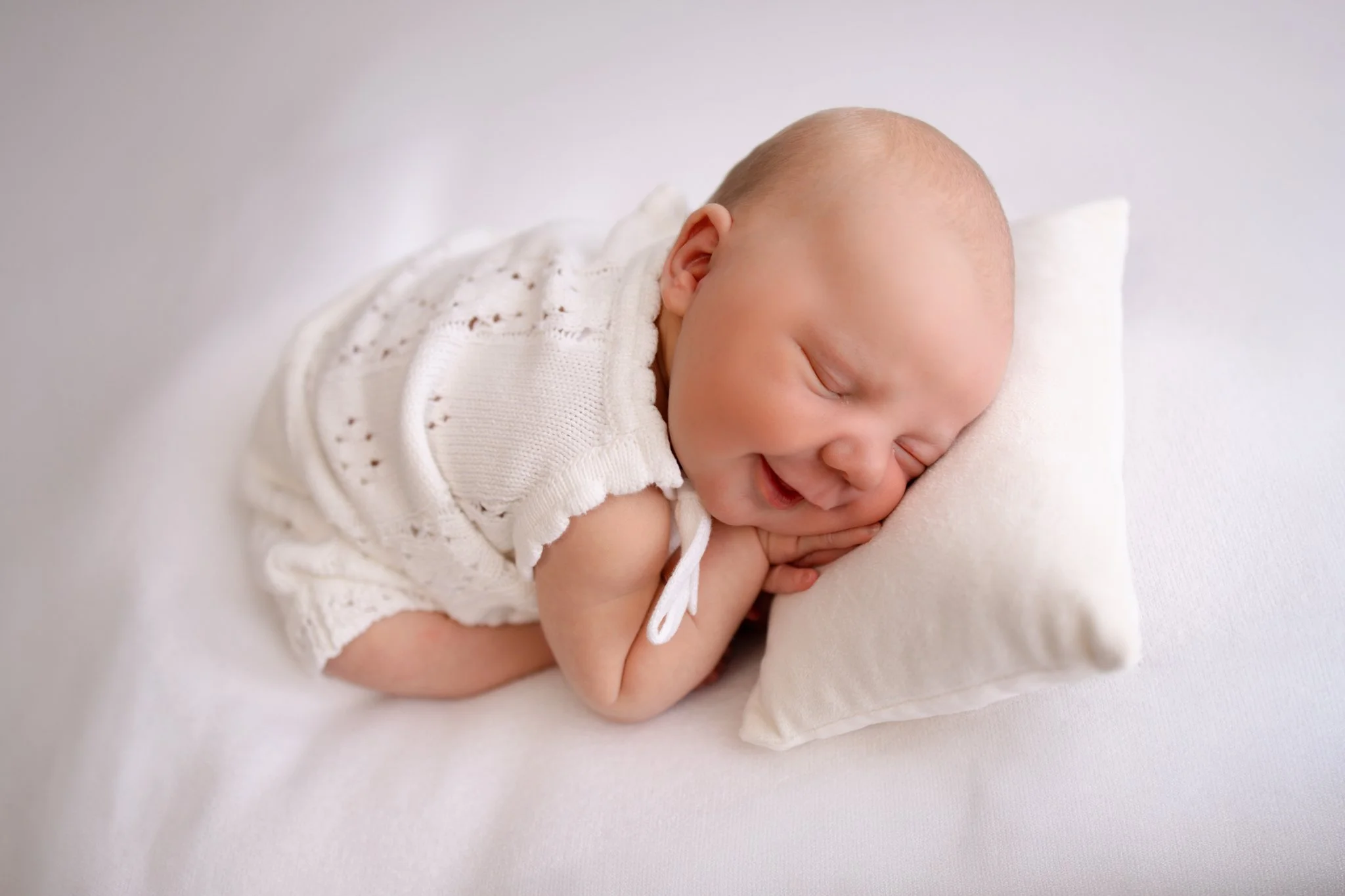 Newborn baby smiling while she sleeps on a small newborn posing pillow at a newborn photography session in Melton West