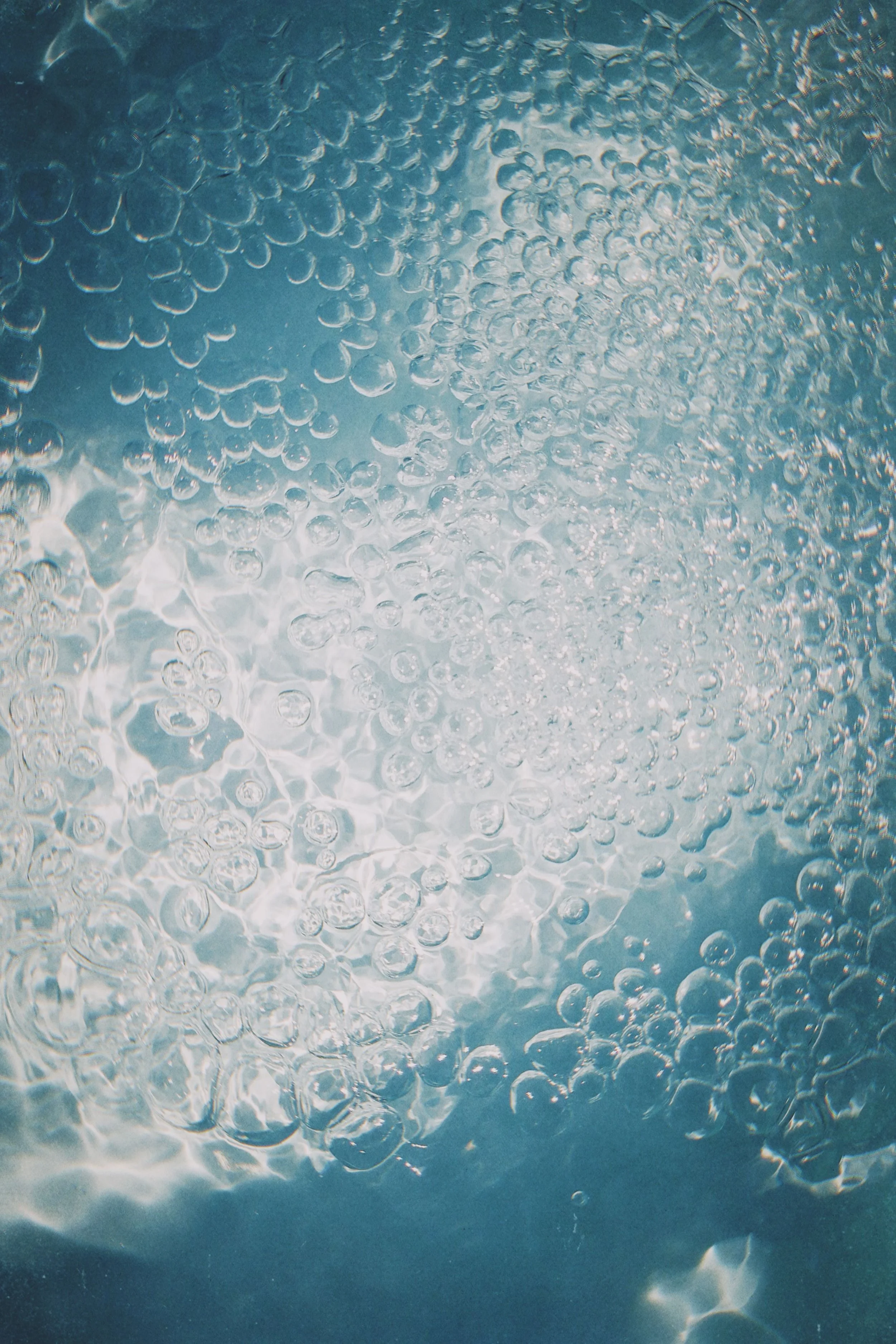 Underwater view showing many bubbles rising toward the surface of the water with sunlight filtering through.