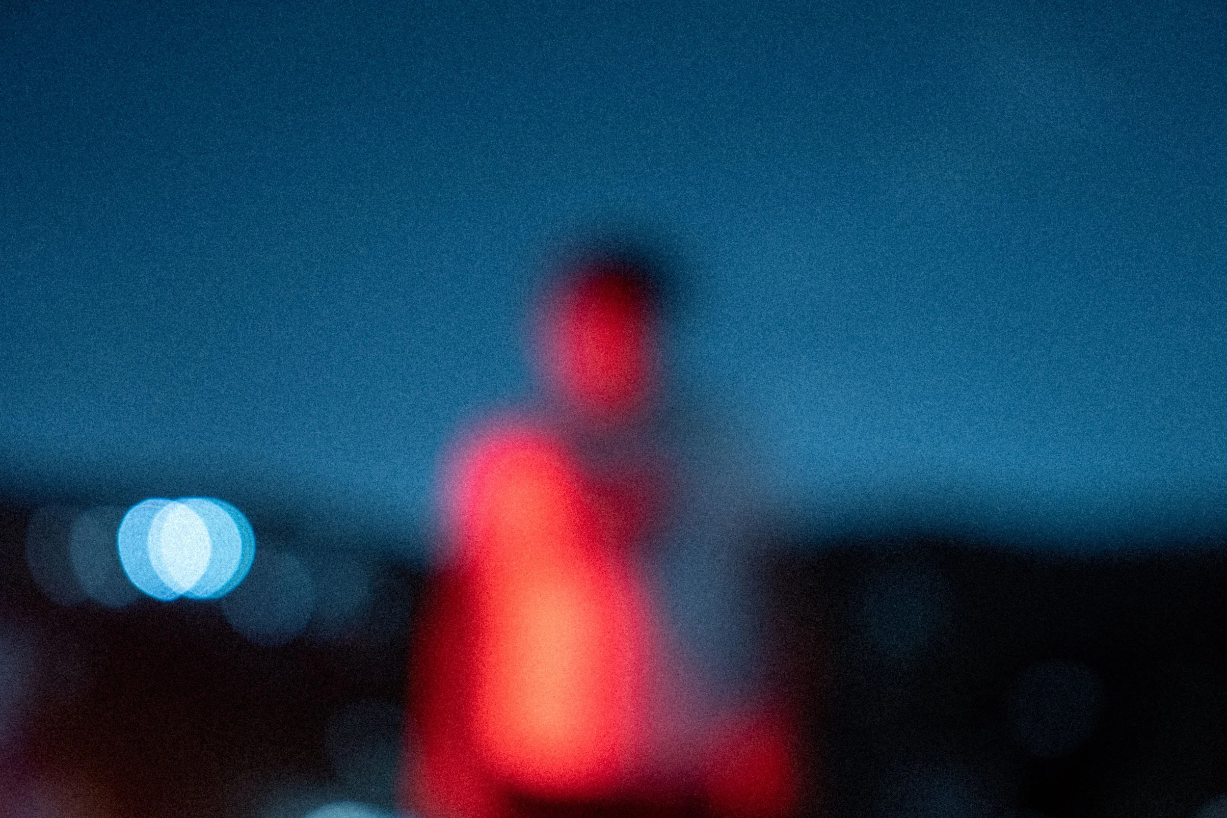 A blurry image with blue and red lights, likely city lights at night, with indistinct shapes and colors.