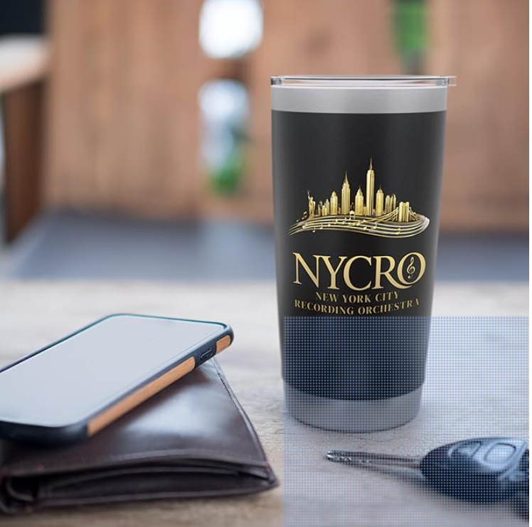 A travel tumbler with NYC skyline and NYCRG logo, a smartphone on a brown wallet, and a car key on a gray surface near a wooden background.