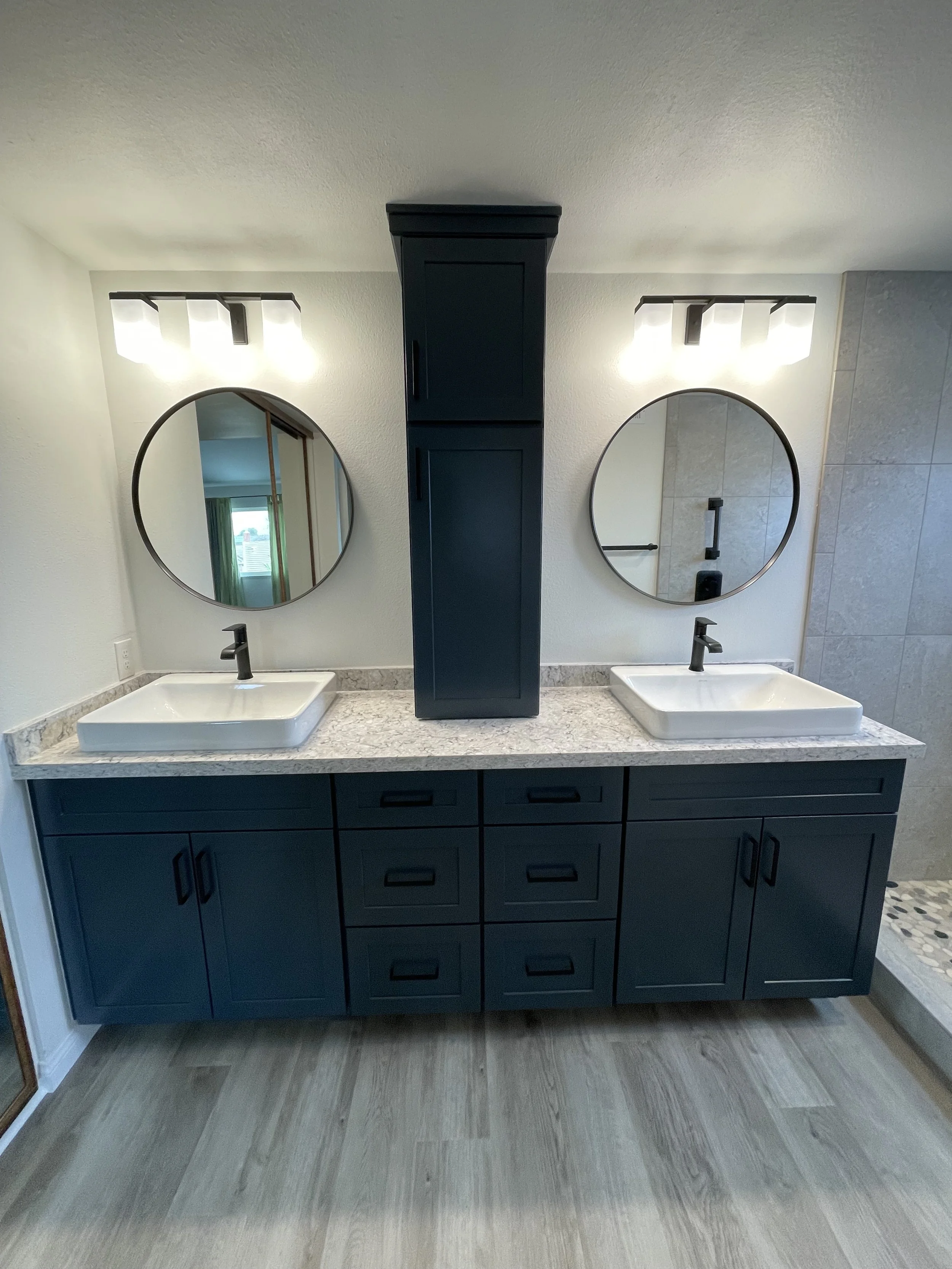 Double sink bathroom vanity with black cabinets, granite countertop, two round mirrors, black fixtures, and two wall-mounted light fixtures.