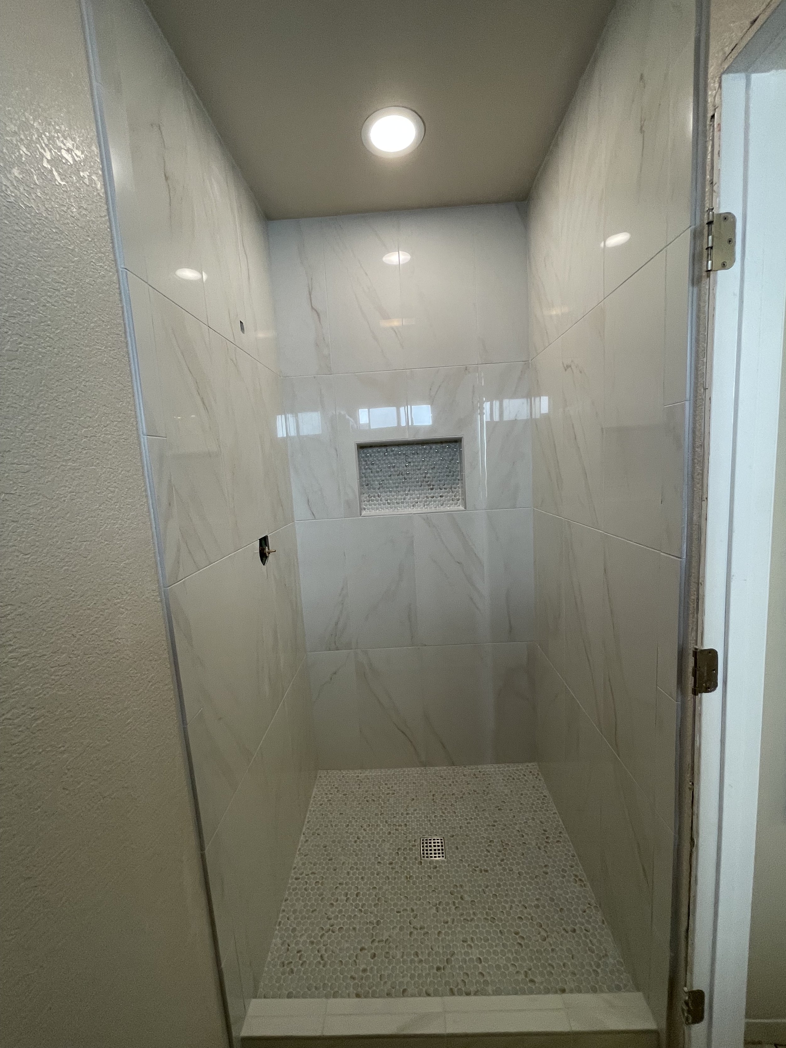 A small shower with tiled walls, a pebble floor, a central drain, and a wall vent in a modern bathroom.